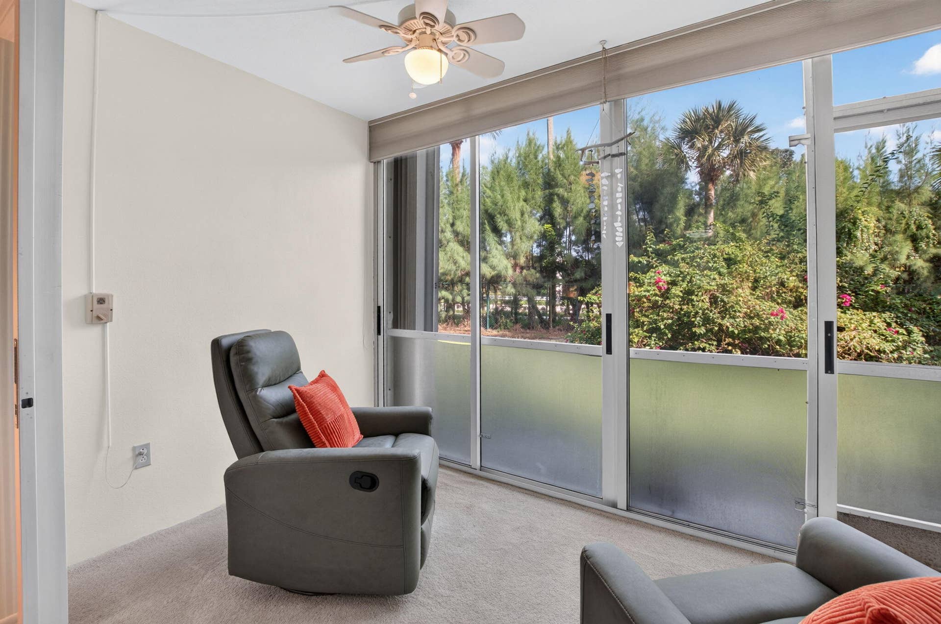 2320 SW 22nd Avenue, #211, Delray Beach, FL 33445 Sunlit sitting room with expansive sliding glass doors opening to landscaped grounds featuring mature trees and tropical vegetation