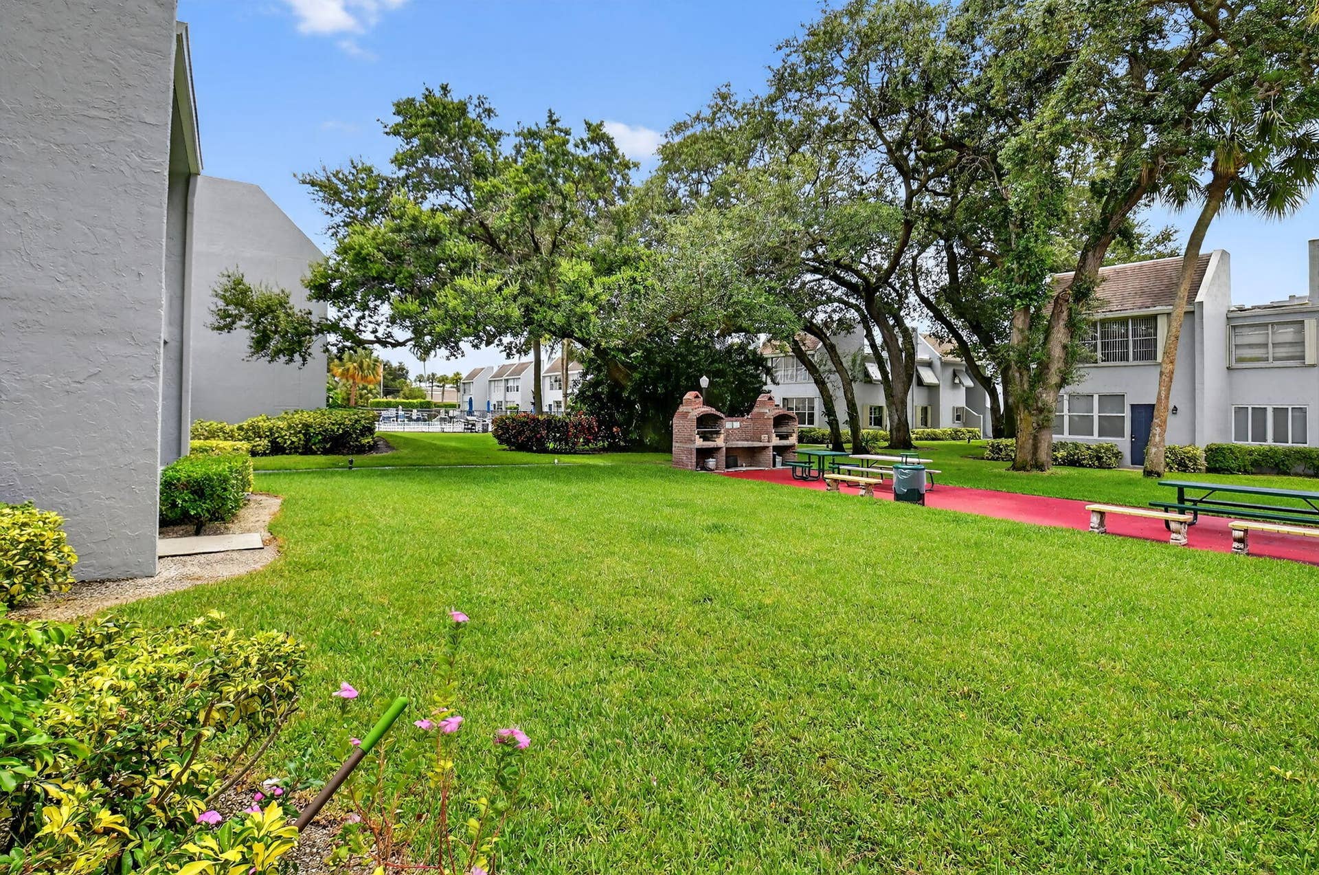 2320 SW 22nd Avenue, #211, Delray Beach, FL 33445 Expansive green space featuring mature trees, a designated barbecue area with two built-in grills, and picnic benches