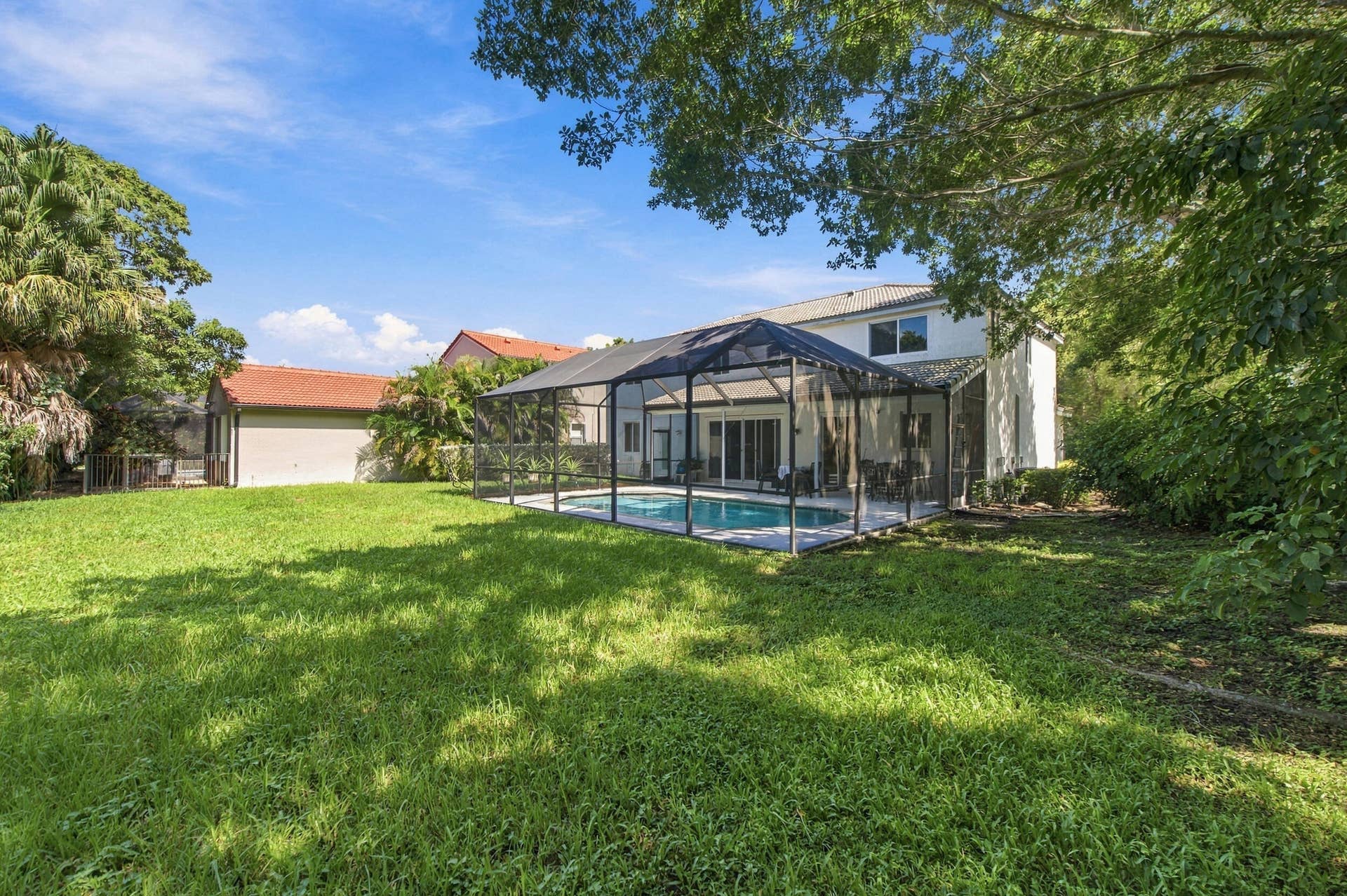 1985 Landing Way, Weston, FL 33326 Expansive backyard with a screened pool enclosure, mature trees, and a two-story residence featuring multiple windows and a covered patio