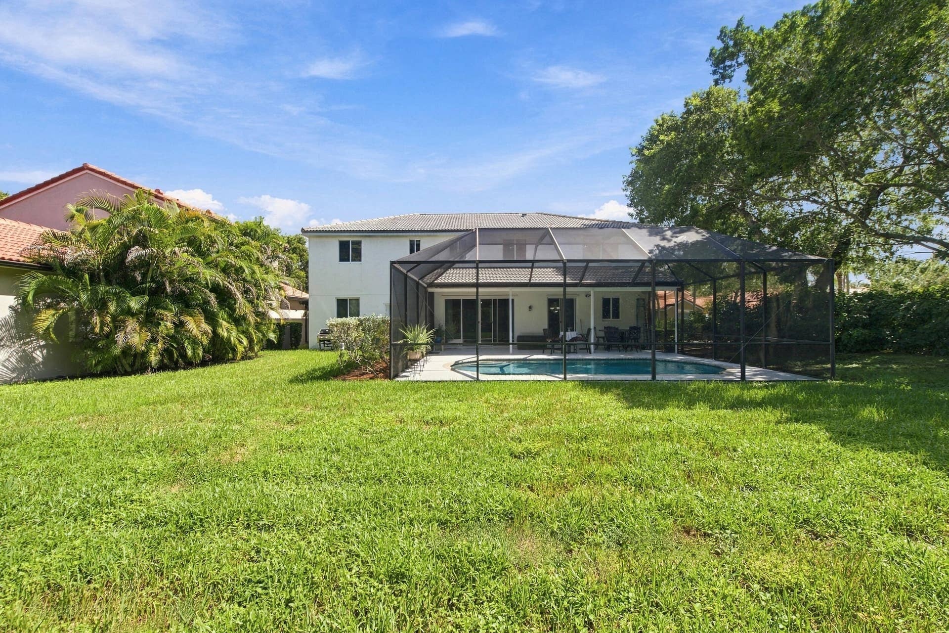 1985 Landing Way, Weston, FL 33326 Expansive backyard featuring a screened pool enclosure, paved patio, and mature landscaping