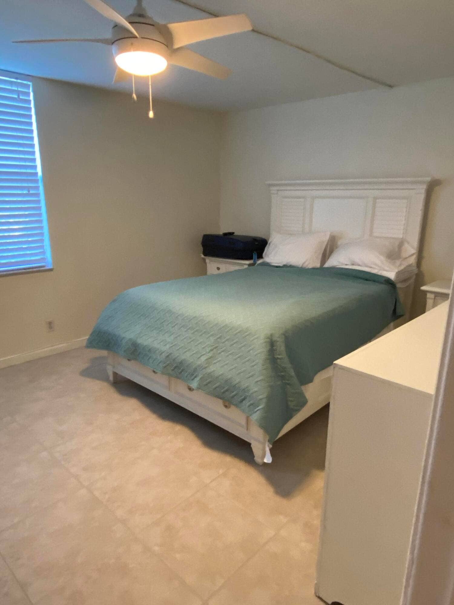 White louvered headboard, tiled flooring, and a ceiling fan with integrated lighting