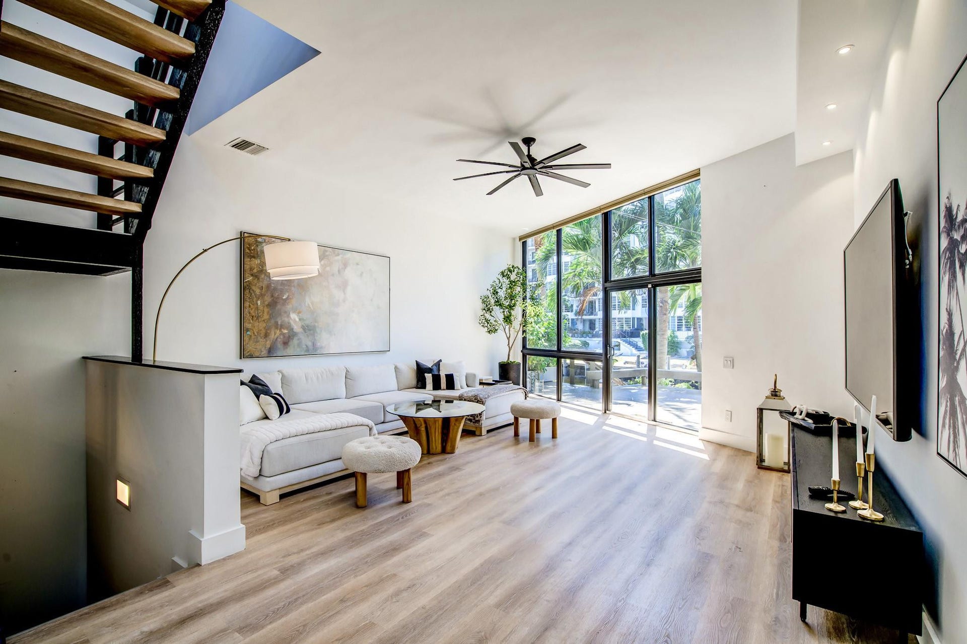 Expansive living area with high ceilings, wood-finish flooring, a contemporary ceiling fan, and extensive floor-to-ceiling windows