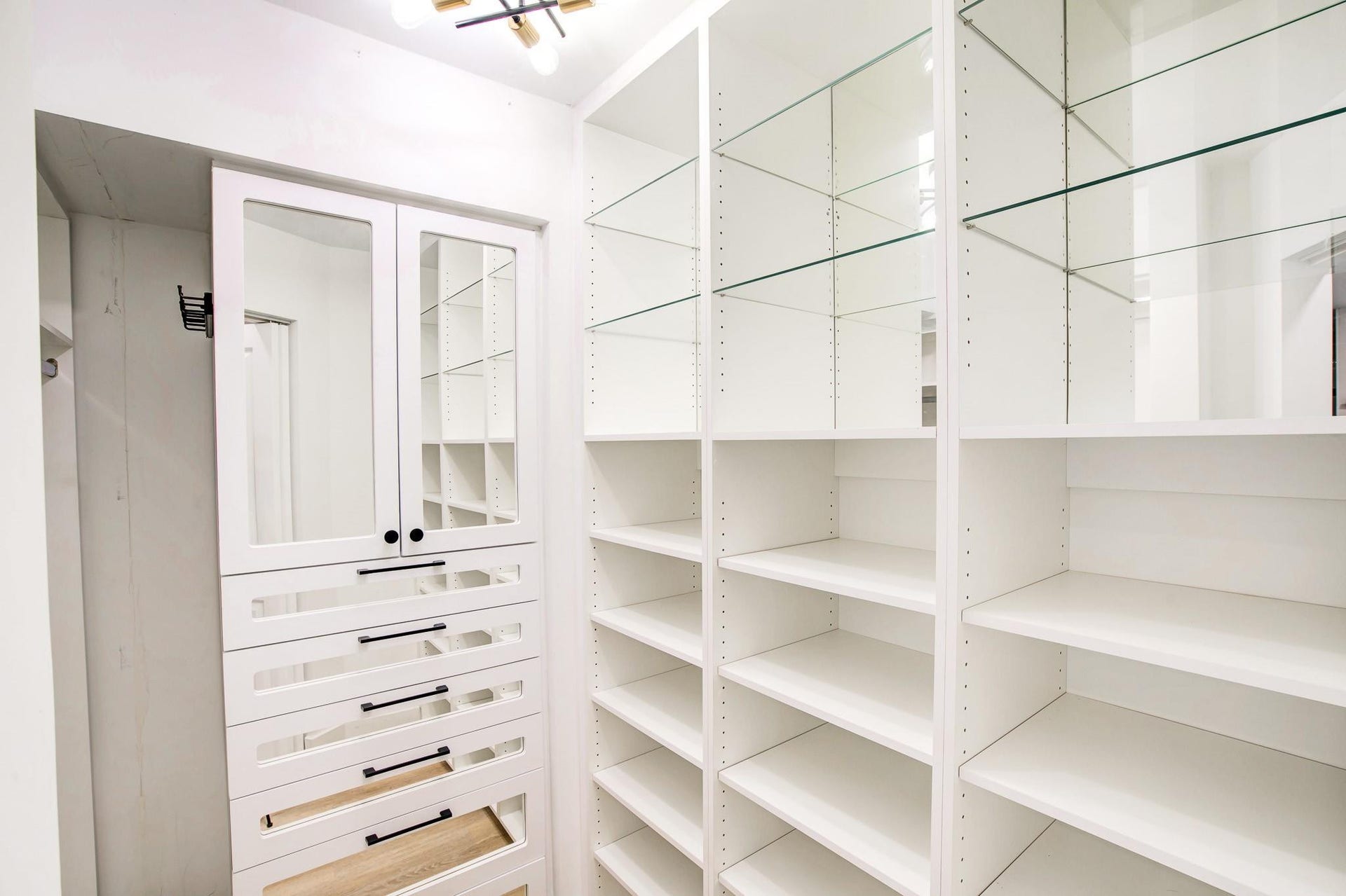 Built-in white storage cabinetry featuring glass-front doors, multiple drawers with dark hardware, adjustable shelving, and glass display shelves
