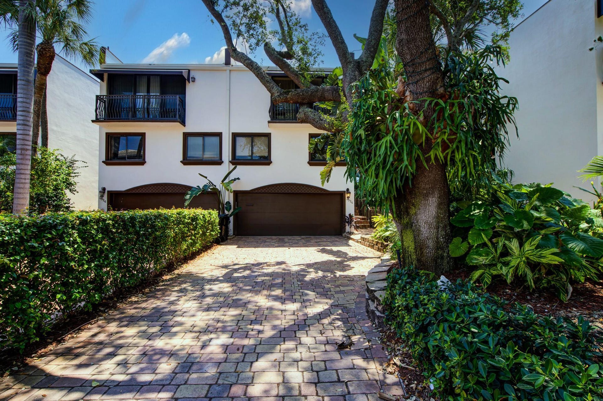 Paver driveway leading to dual garage doors, featuring a stucco exterior with decorative window trim, and multiple wrought iron balconies