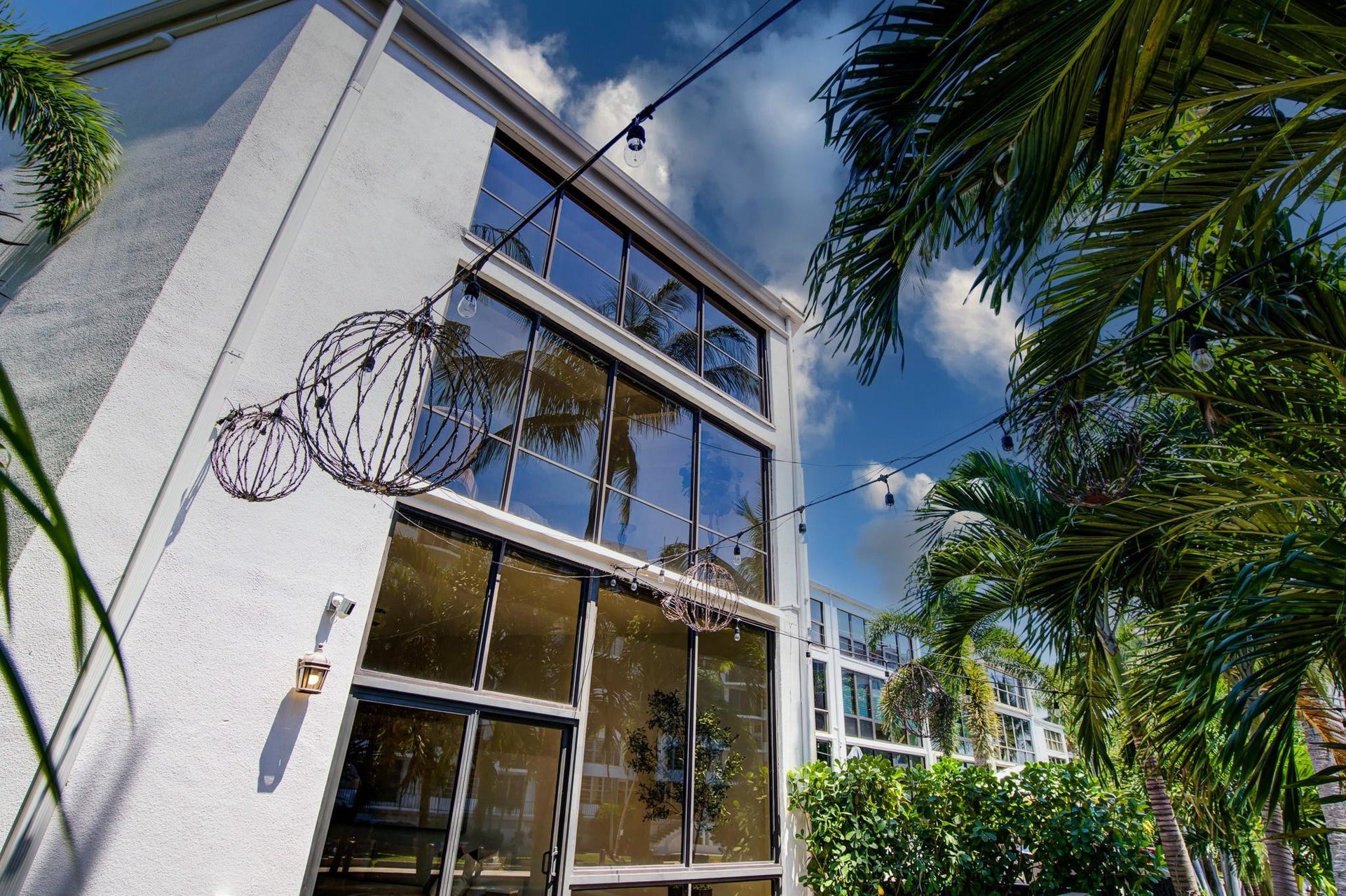 Contemporary architectural design with white stucco facade, expansive multi-story windows, and prominent palm trees