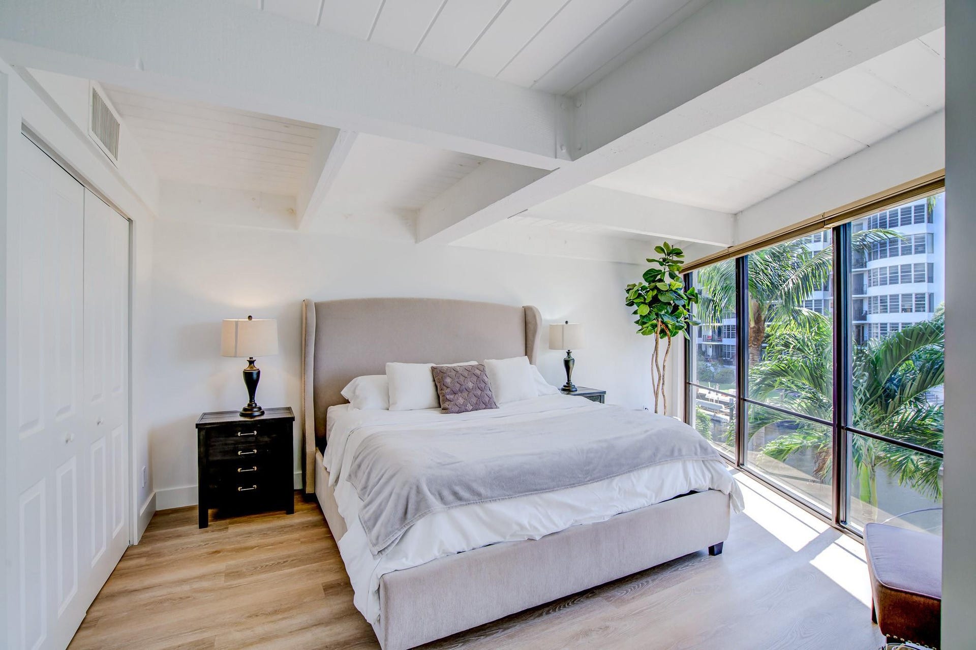 Pitched ceiling with exposed beams, wood-finish flooring, full-height windows, and bi-fold closet doors