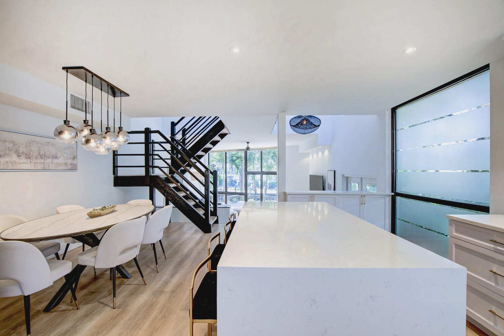 Open-concept living space with wood-finish flooring, a contemporary black staircase, and a large frosted window