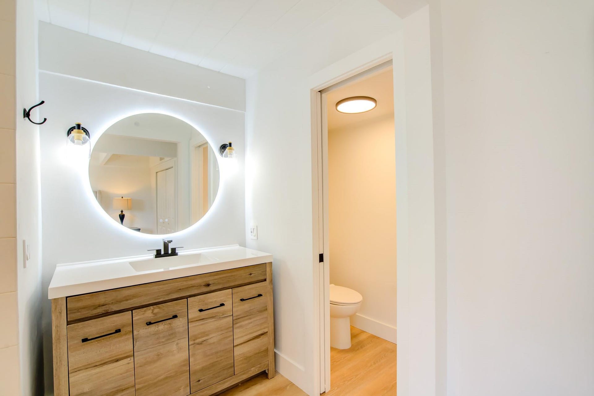 Modern vanity with a circular backlit mirror, integrated sink, and wood-finish cabinetry