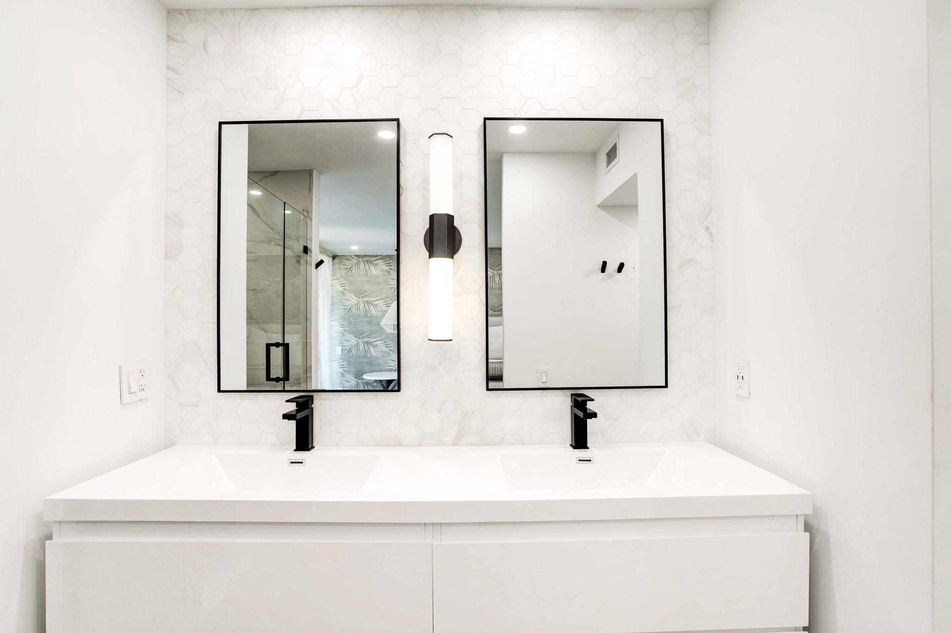 Dual vanity with integrated sinks, matte black faucets, hexagon tile backsplash, and rectangular mirrors with black frames