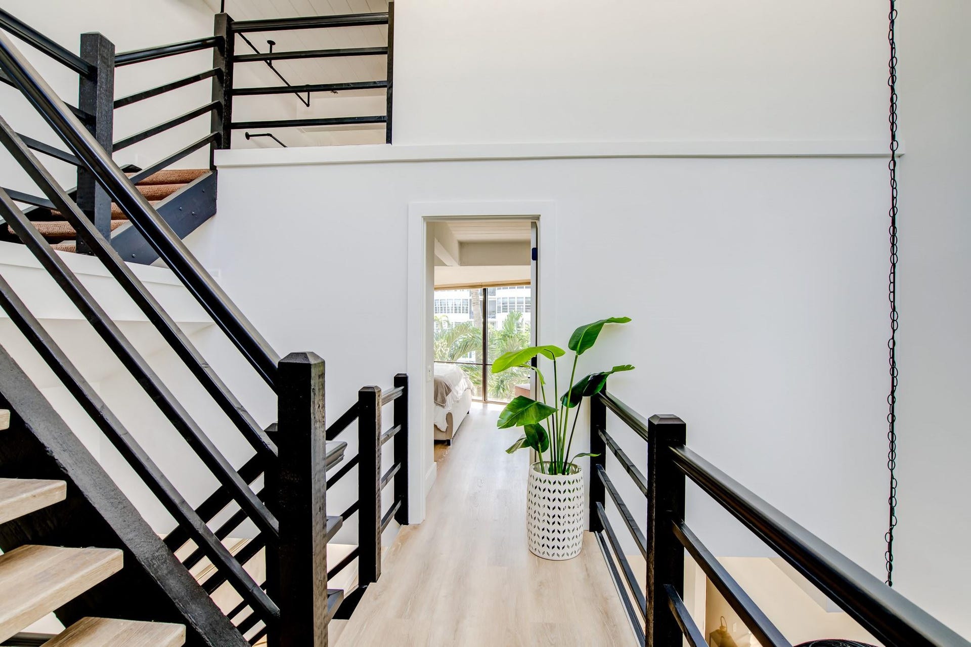 Open-concept interior featuring light wood-finish flooring, a white wall finish, and a black open-tread staircase with wood-finish steps