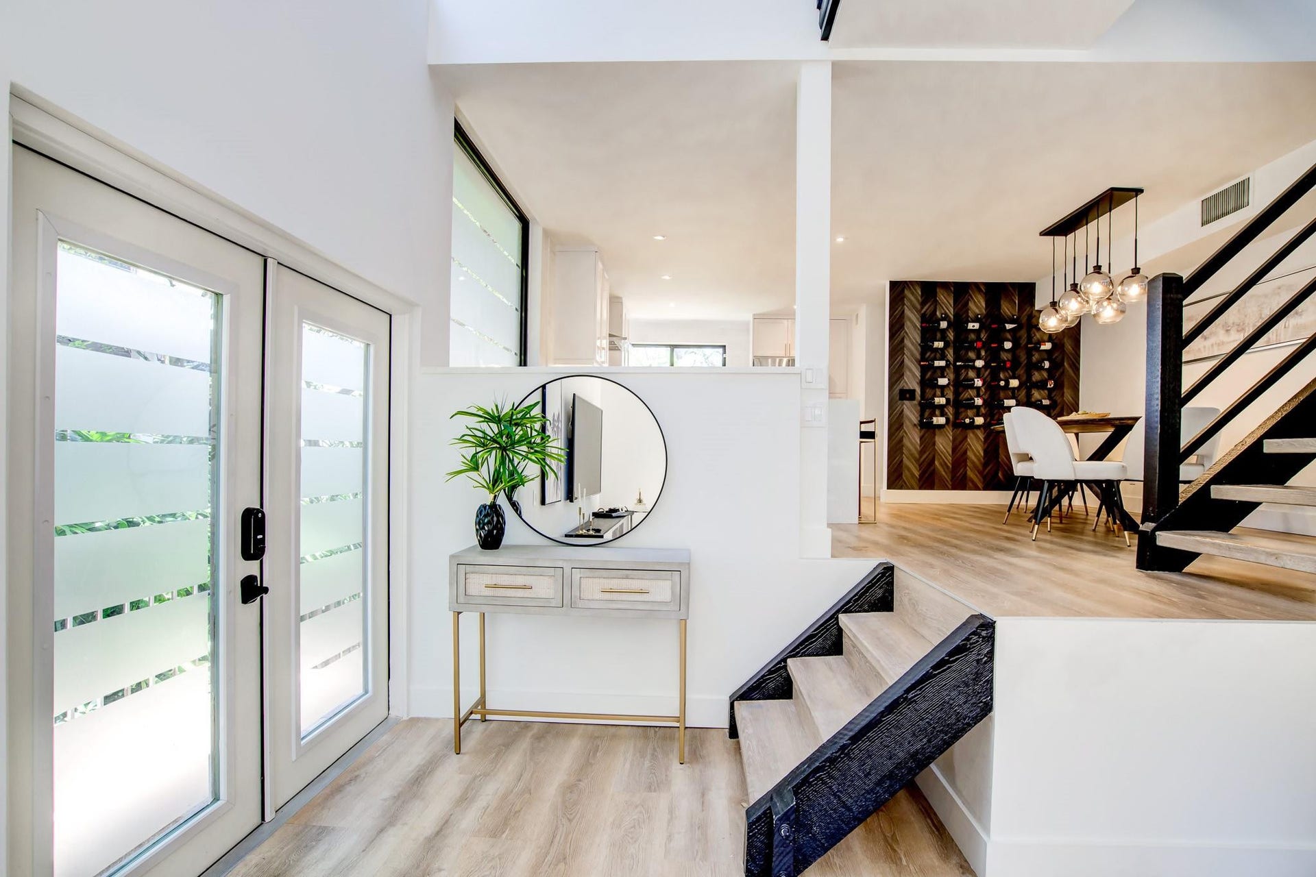 Wood-finish flooring throughout, frosted glass double doors, modern open-riser staircase with black railings, and a built-in wine display