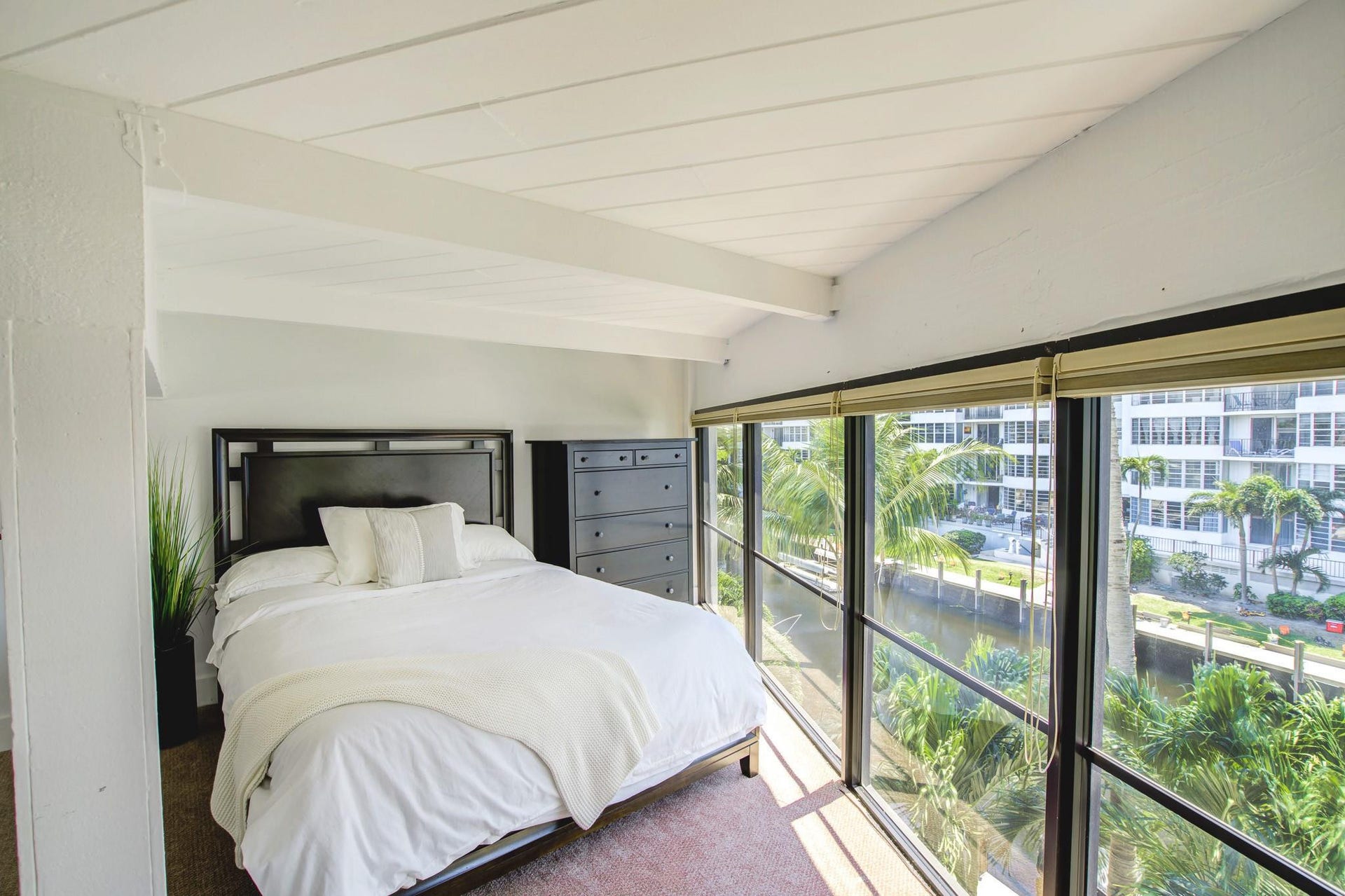 Vaulted ceiling with exposed beams, floor-to-ceiling windows, and roller shades