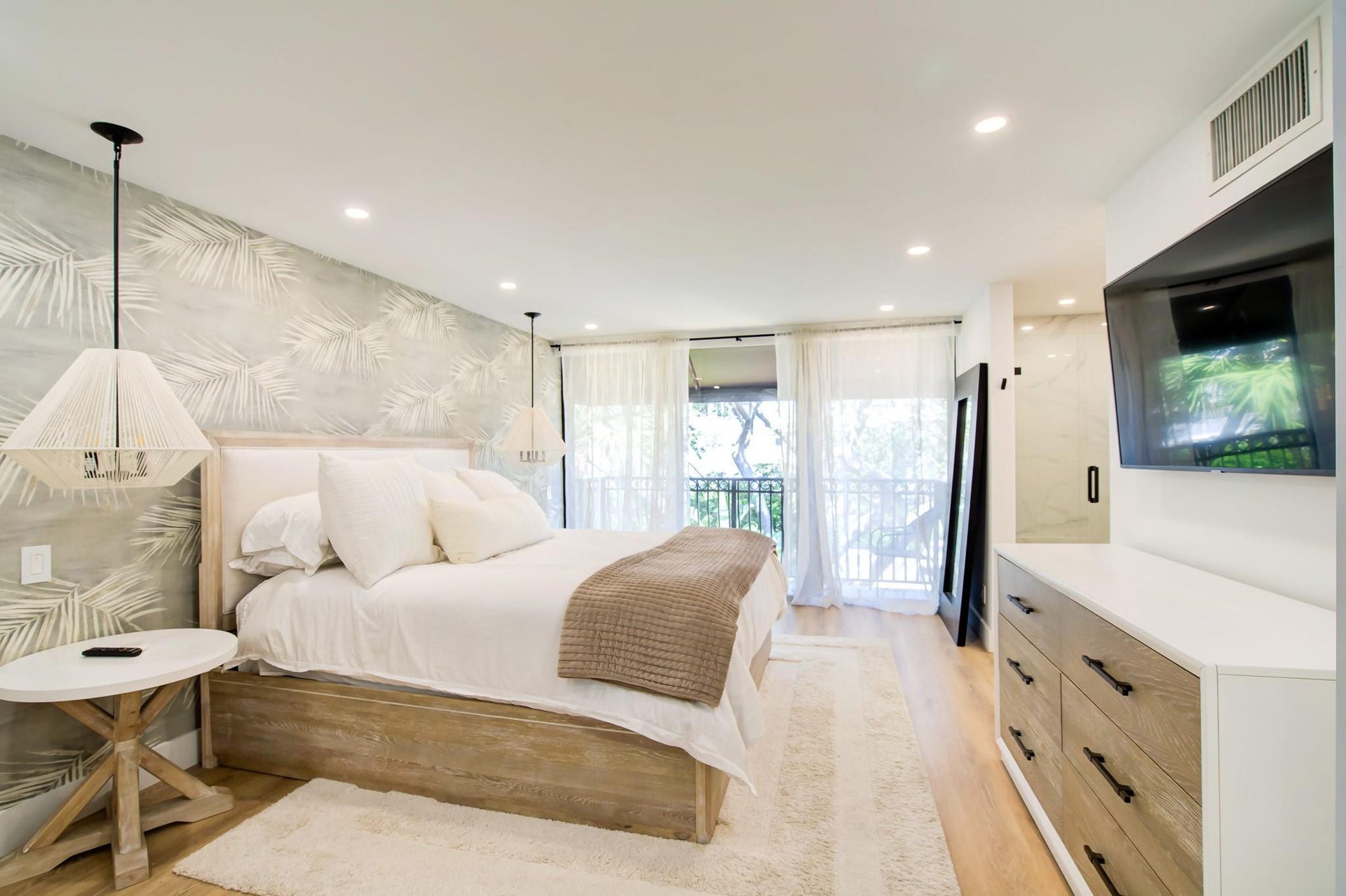 Recessed lighting, wood-finish flooring, accent wall with botanical pattern, full-height glass doors to balcony, and built-in vanity with integrated storage