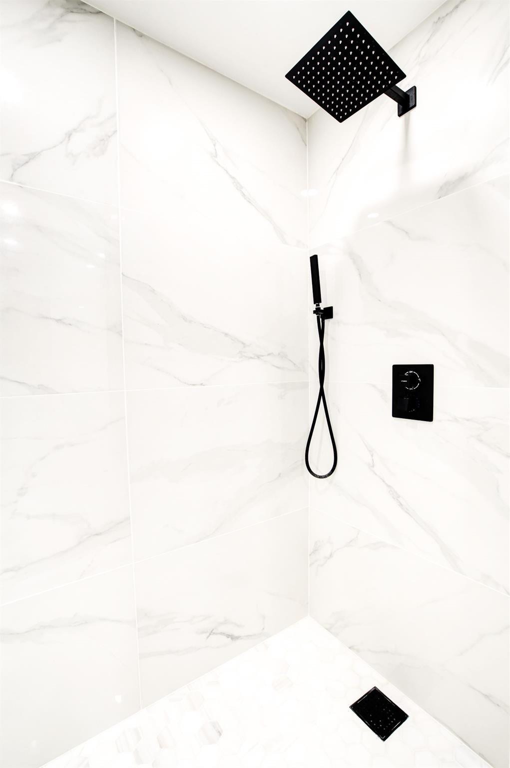 White marble-look wall tiles with square matte black rain shower head and handheld shower
