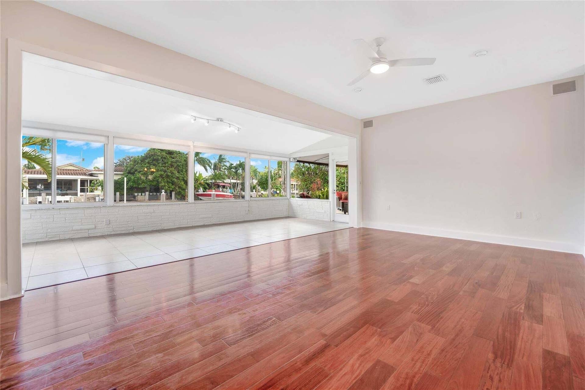 2142 NE 17th Avenue, Wilton Manors, FL 33305 Hardwood flooring in the main room, with an expansive opening to a sunroom featuring large windows, white tile flooring, and track lighting