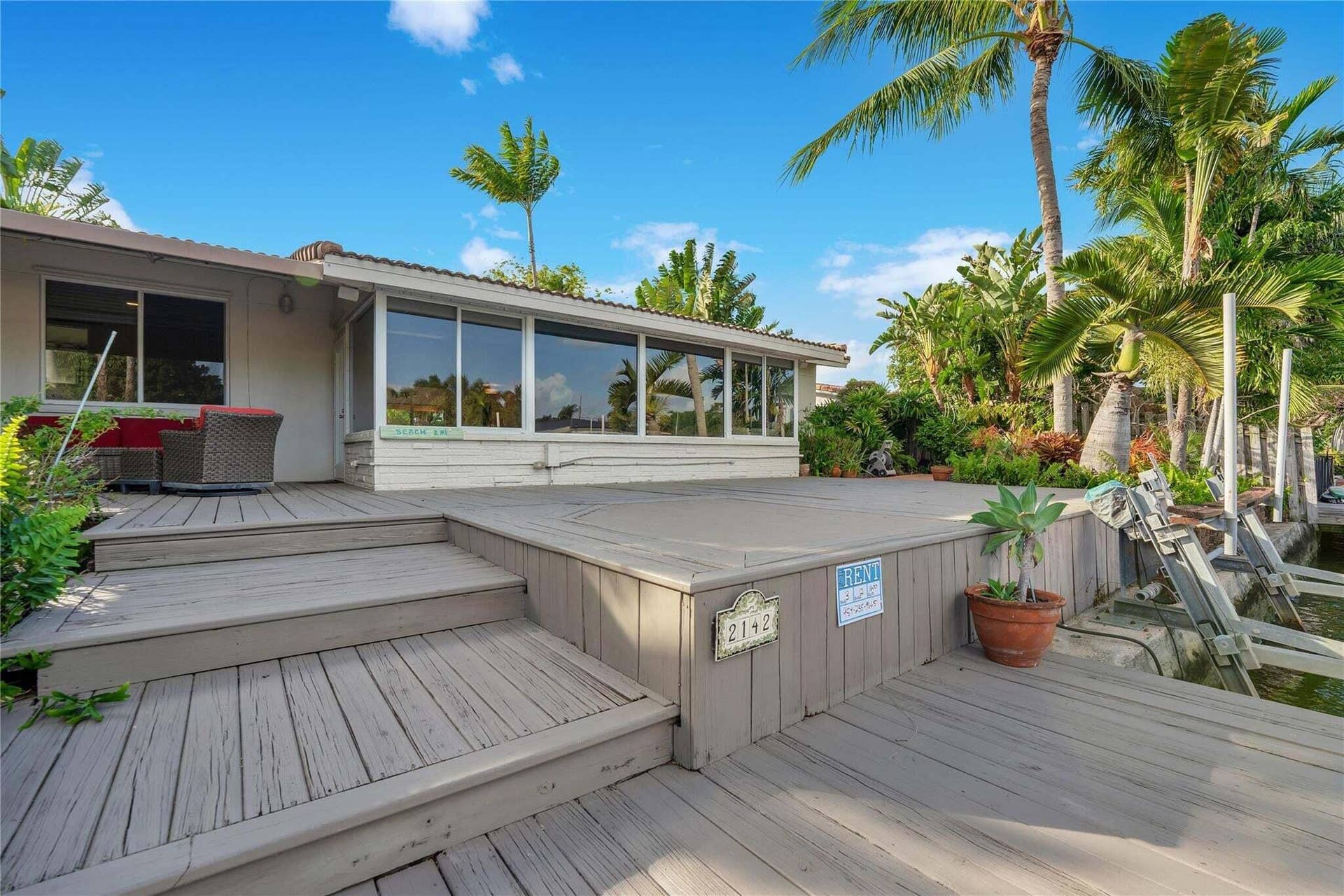 2142 NE 17th Avenue, Wilton Manors, FL 33305 Expansive wood-finish deck with multiple levels, substantial glass panel windows, and lush tropical landscaping