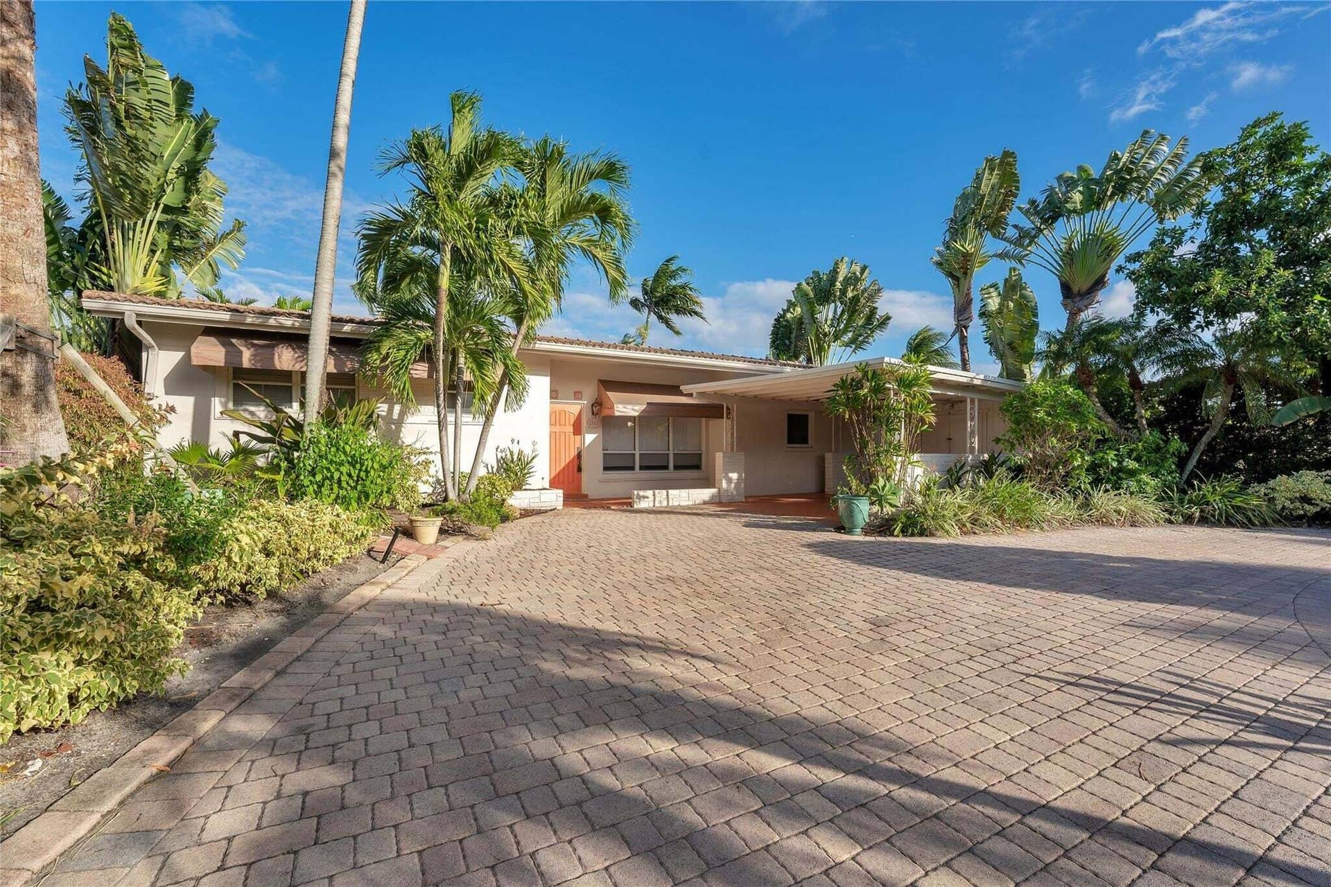 2142 NE 17th Avenue, Wilton Manors, FL 33305 Expansive paver driveway leading to a residence with a covered entryway, decorative awnings, and mature tropical landscaping