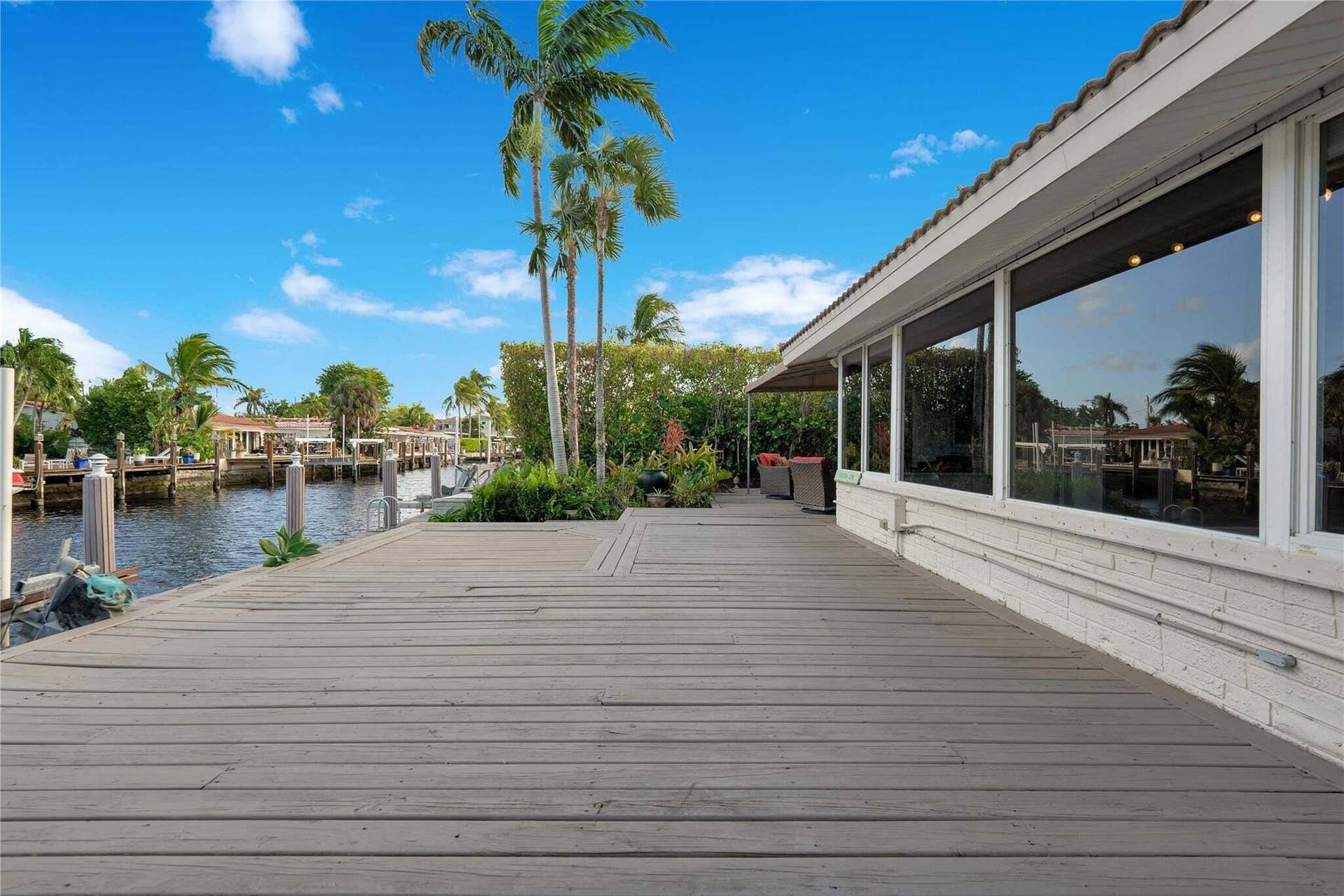 2142 NE 17th Avenue, Wilton Manors, FL 33305 Waterfront property featuring a spacious deck, multiple dock pilings, a white brick exterior, and large picture windows