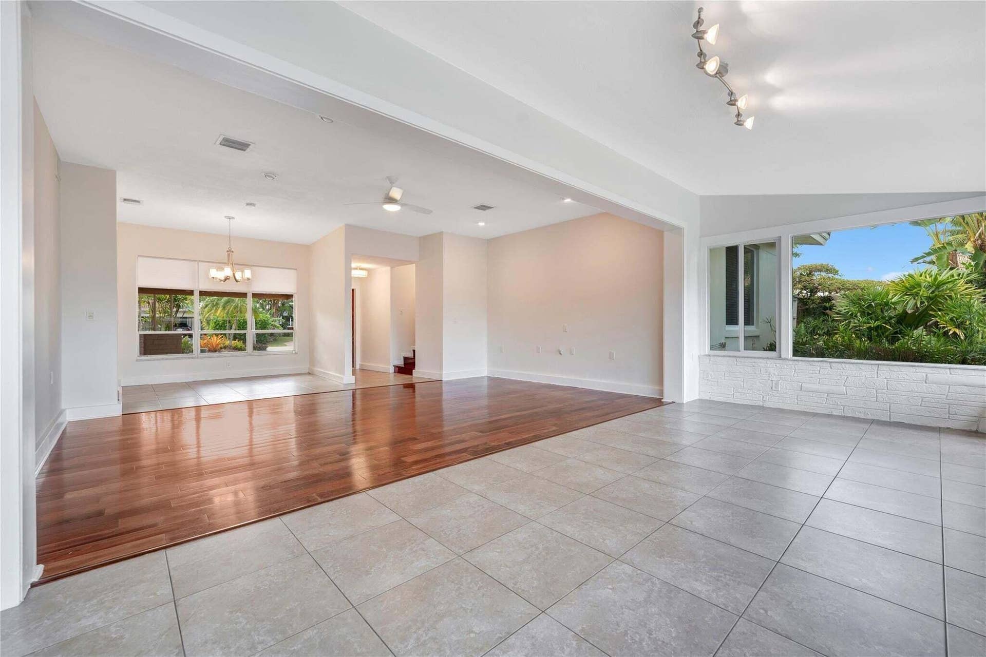 2142 NE 17th Avenue, Wilton Manors, FL 33305 Expansive interior featuring large format tile flooring and wood-finish flooring, with a dining area illuminated by a chandelier and a sunroom with white brick paneling and track lighting