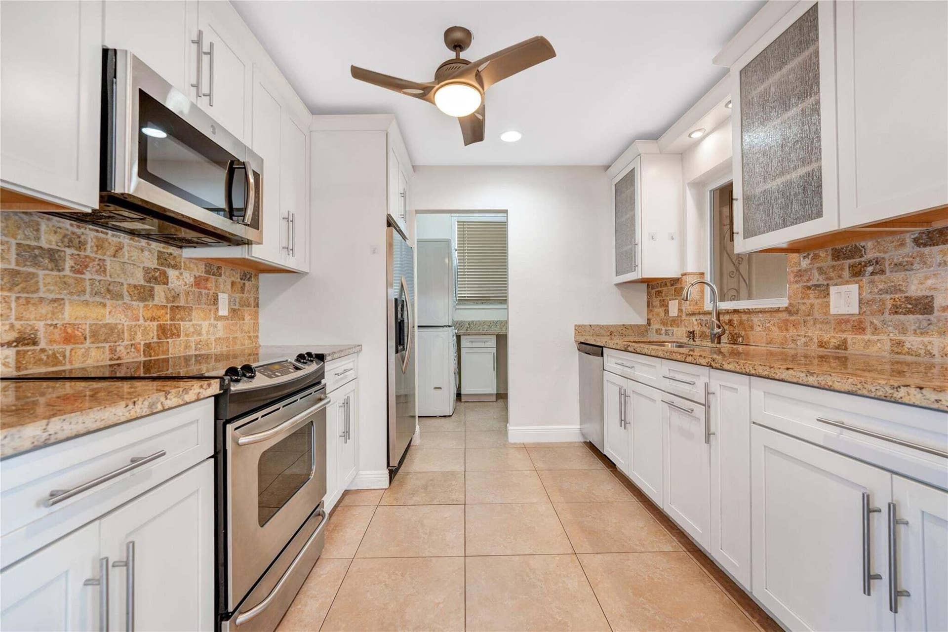 2142 NE 17th Avenue, Wilton Manors, FL 33305 Kitchen featuring white cabinetry, stone tile backsplash, stainless steel appliances, granite countertops, and ceiling fan with integrated lighting
