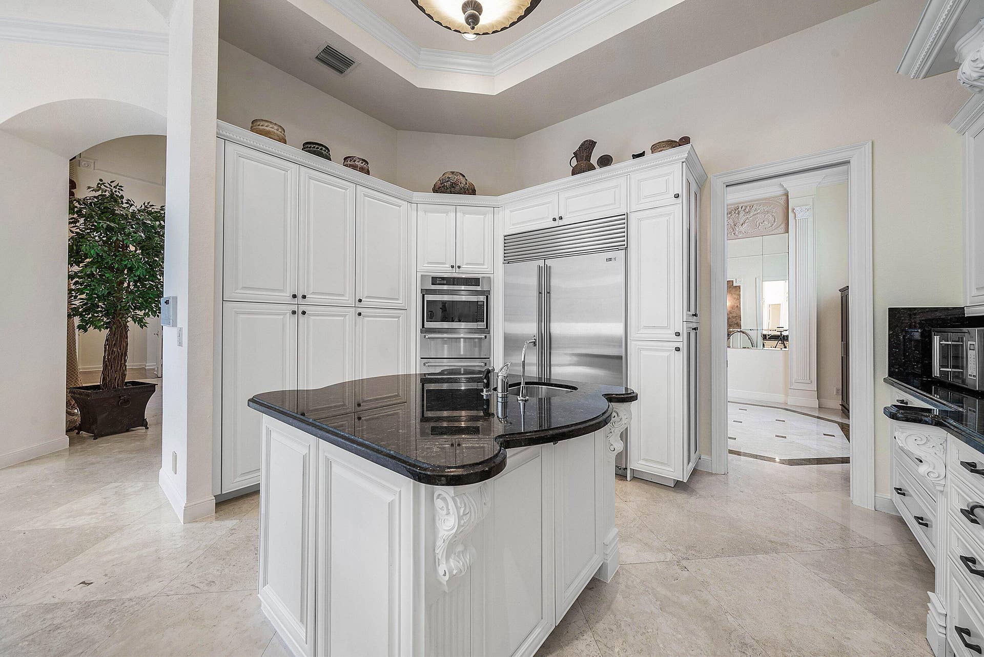 White paneled cabinetry, curved granite island with integrated sink, Sub Zero fridge, Thermador wall oven.