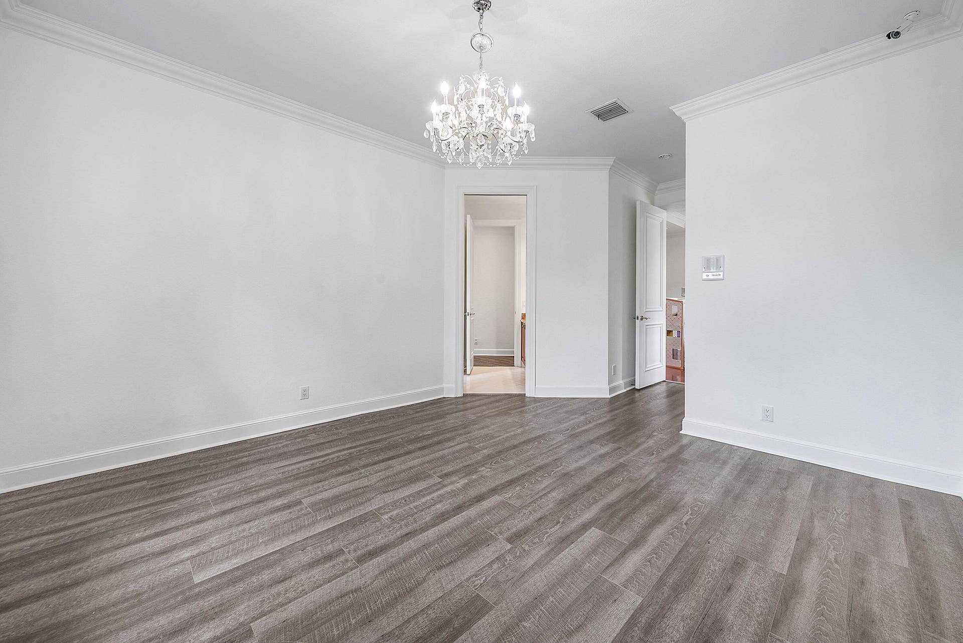 Wood-finish flooring, crown molding, white paneled doors leading to shared bathroom