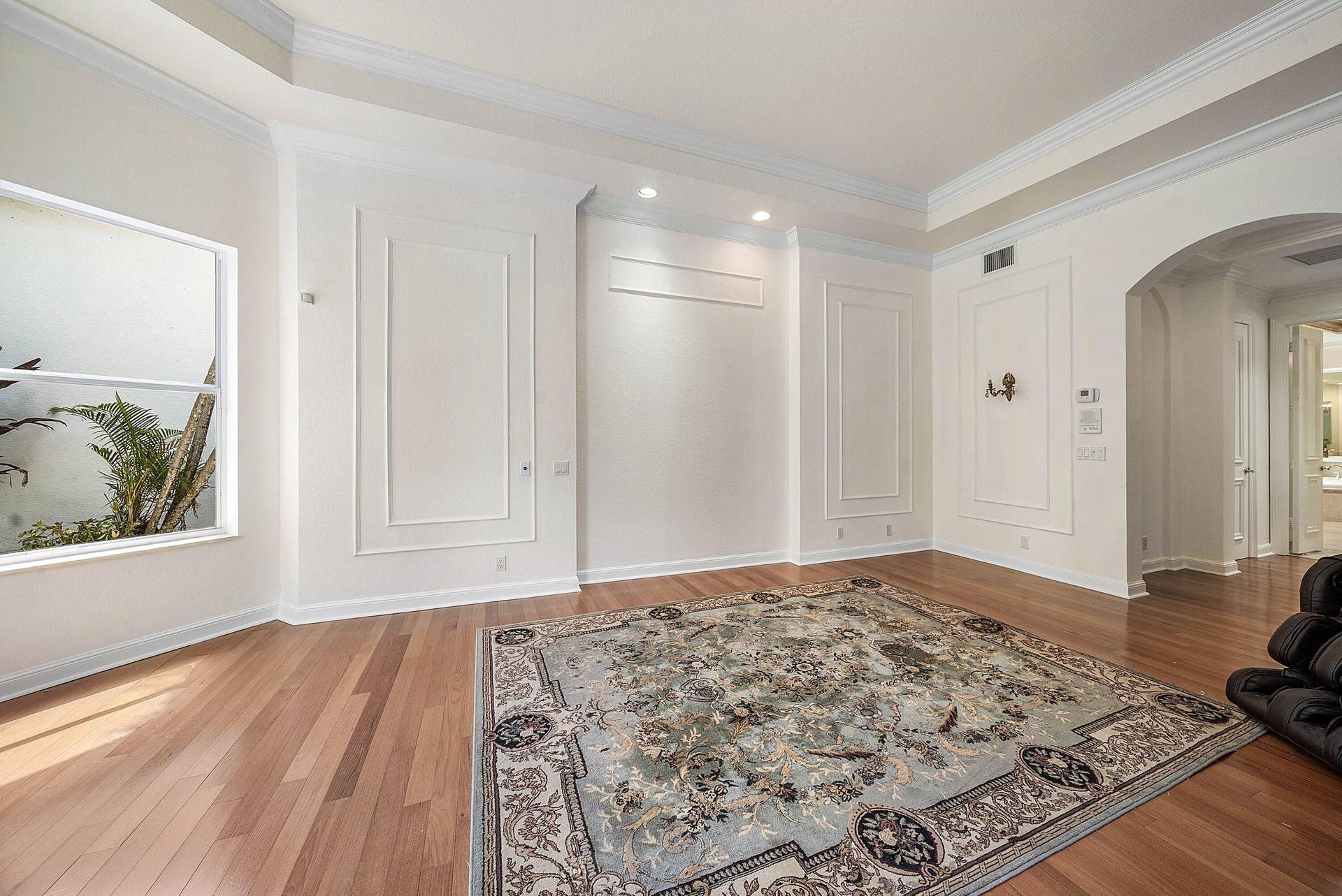 Primary bedroom features engineered Hardwood flooring, arched doorway, recessed lighting, crown molding, and decorative wall paneling