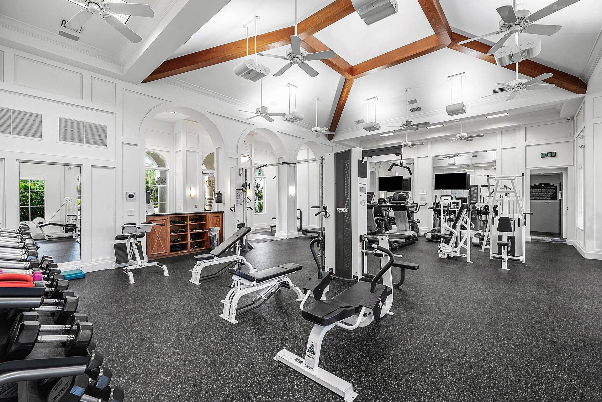 High vaulted ceiling with exposed wood beams, multiple ceiling fans, wide range of fitness equipment