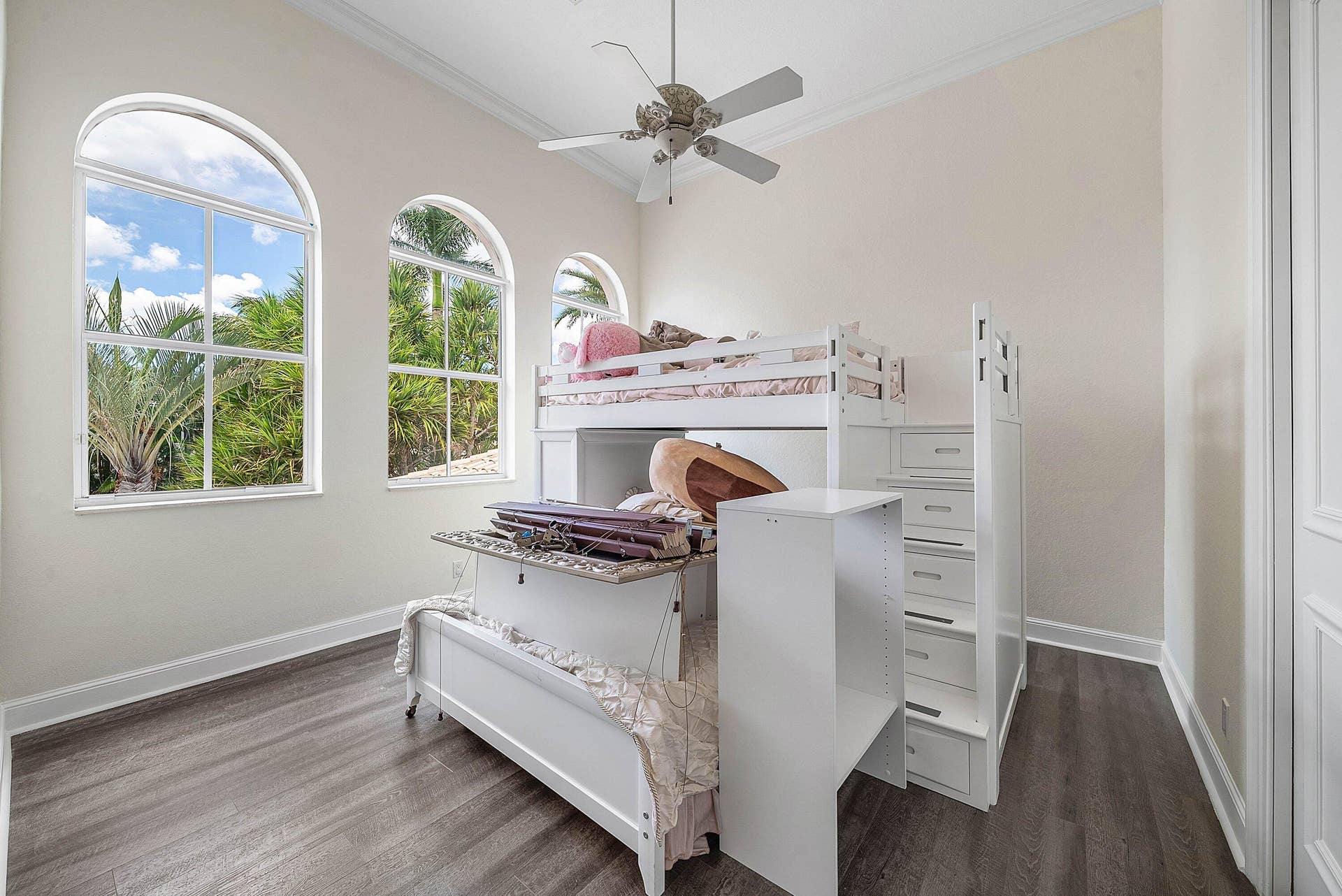 Vaulted ceiling with a ceiling fan, arched windows, and wood-finish flooring