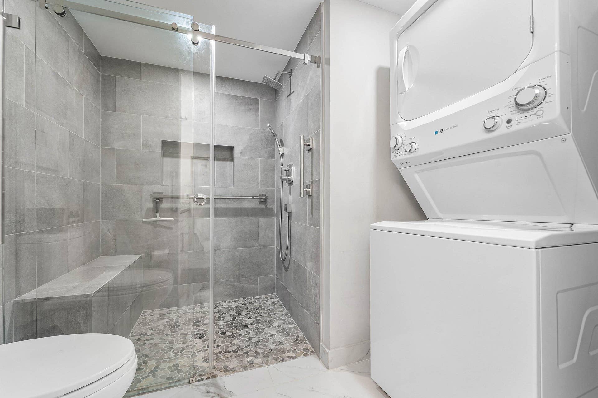 12 Stratford Drive E, #A, Boynton Beach, FL 33436 Glass-enclosed shower with a built-in bench, pebble-tiled floor, and a recessed niche