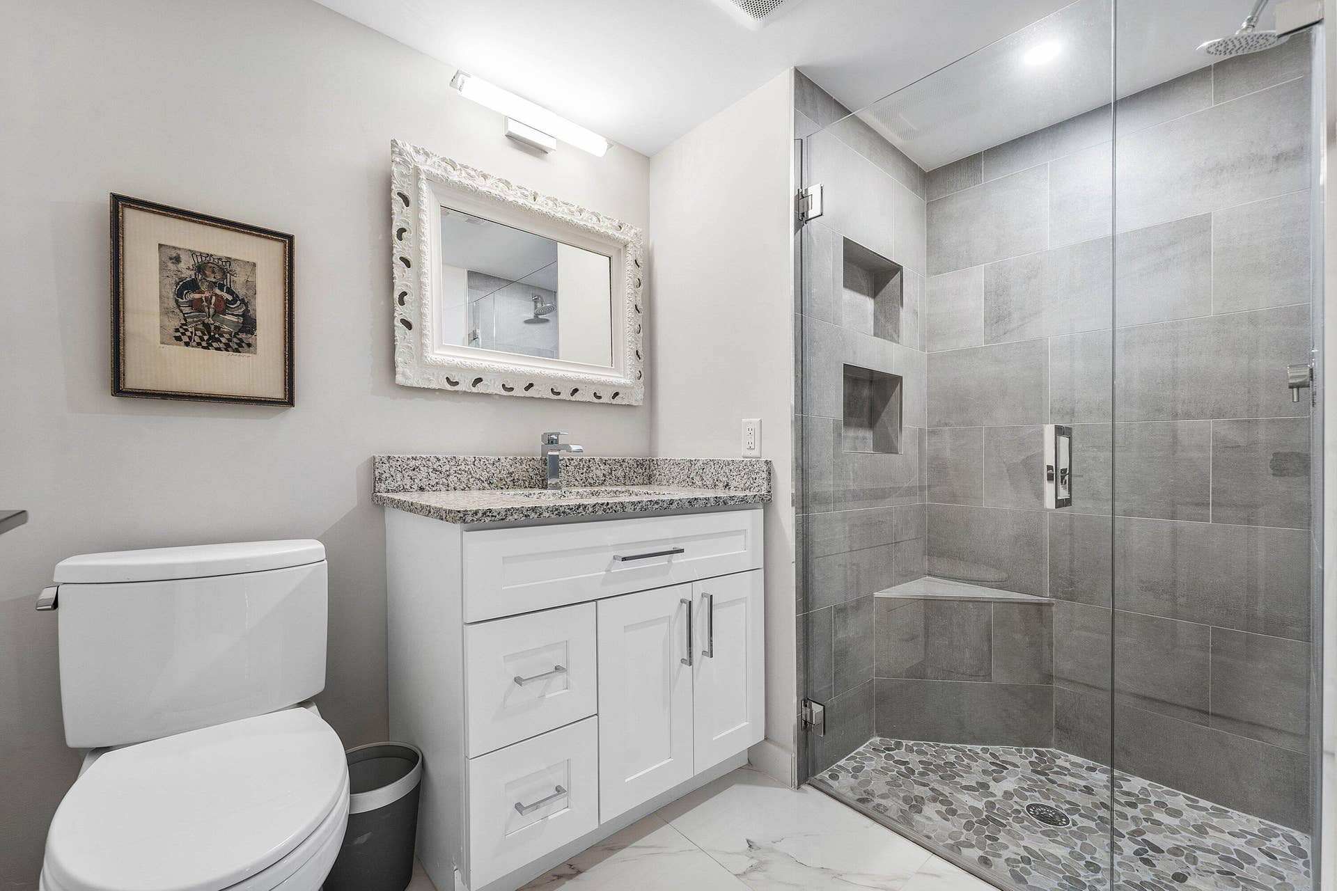 12 Stratford Drive E, #A, Boynton Beach, FL 33436 White vanity with granite countertop, glass-enclosed shower, tiled shower walls with recessed niches, pebble-tiled shower floor, and tile flooring