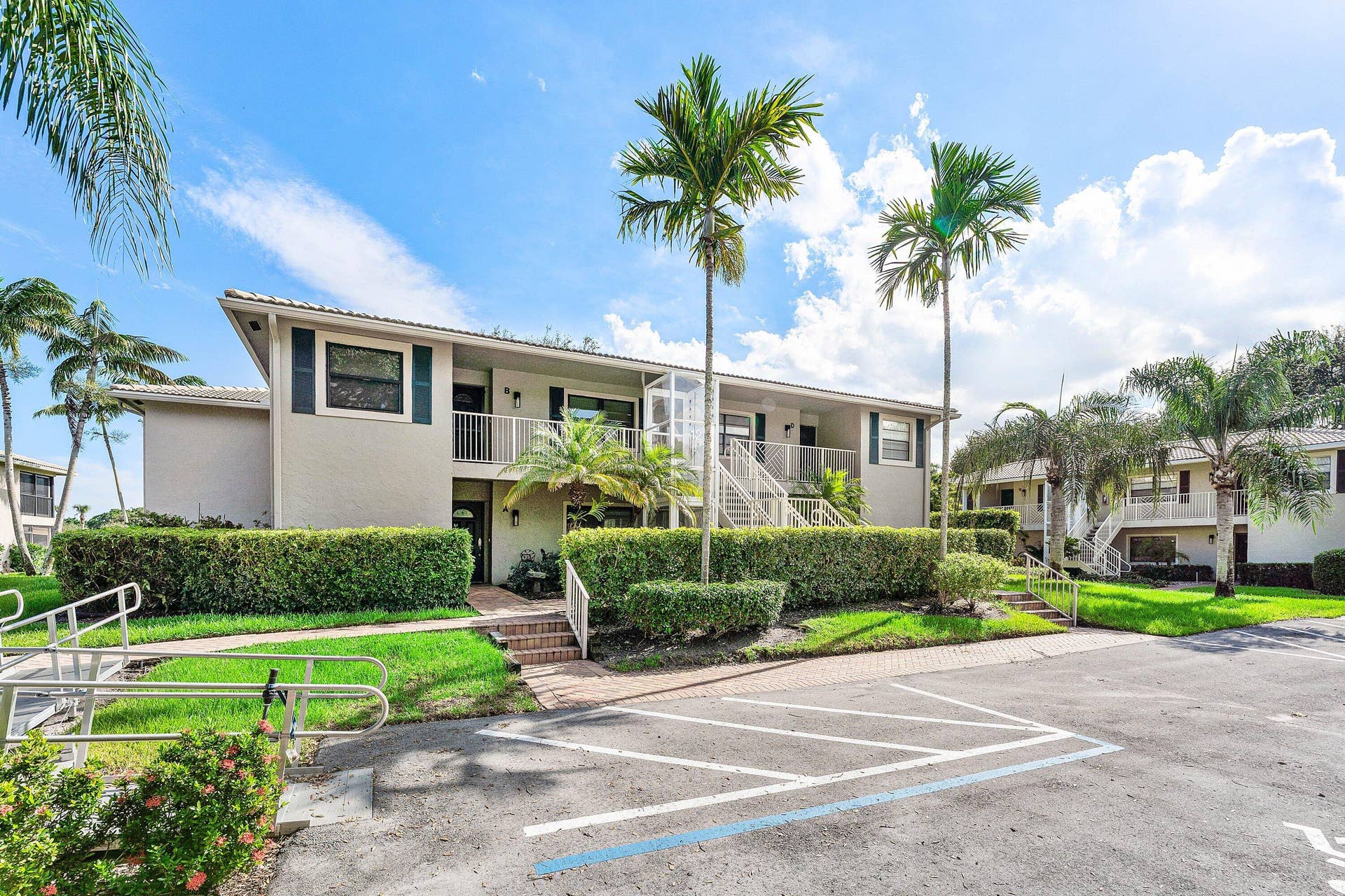 12 Stratford Drive E, #A, Boynton Beach, FL 33436 Two-story building with exterior access, featuring mature palm trees, manicured hedges, and brick pathways