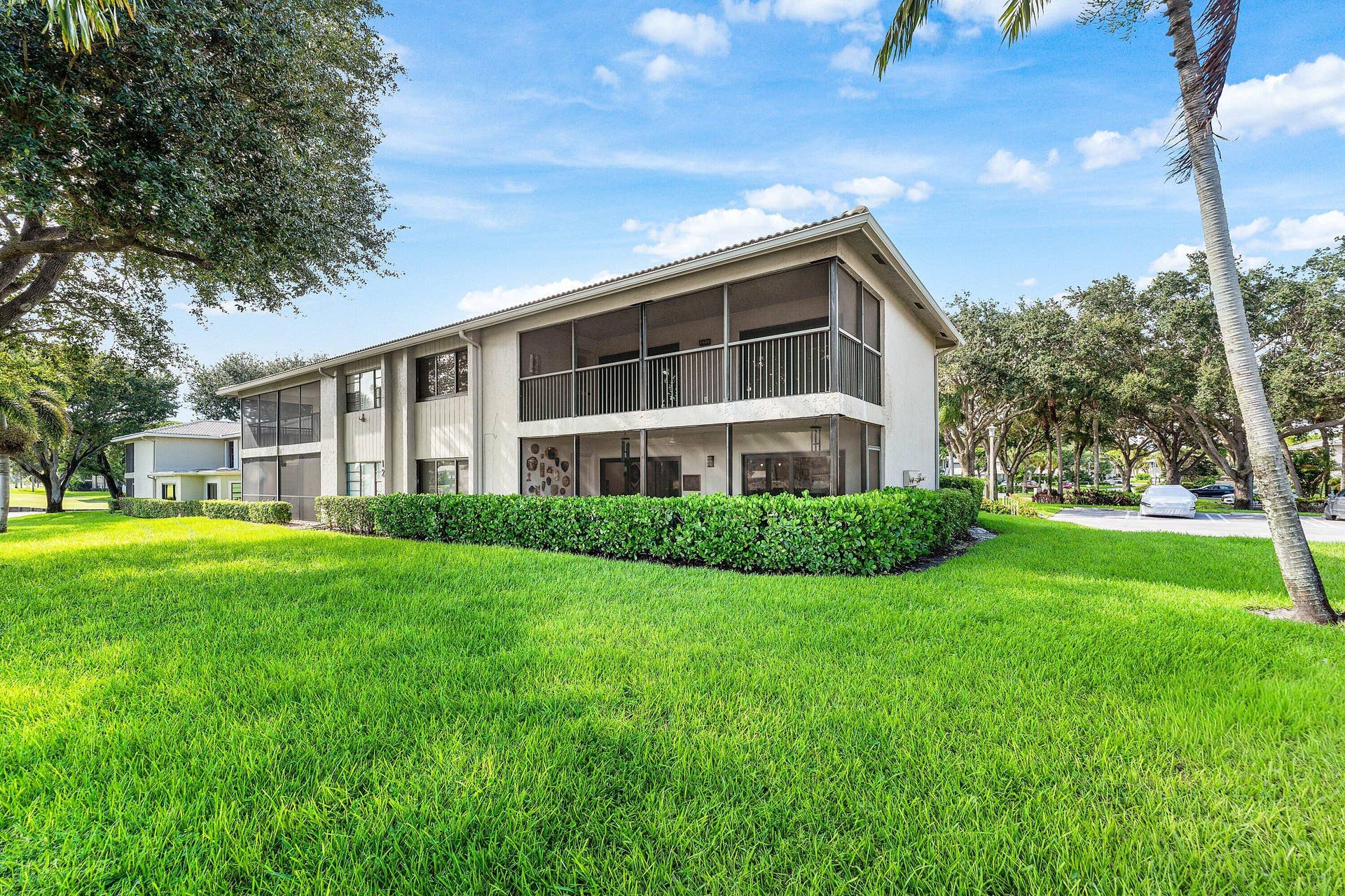 12 Stratford Drive E, #A, Boynton Beach, FL 33436 Two-story exterior with screened-in upper balcony, screened-in lower patio, and manicured shrubbery
