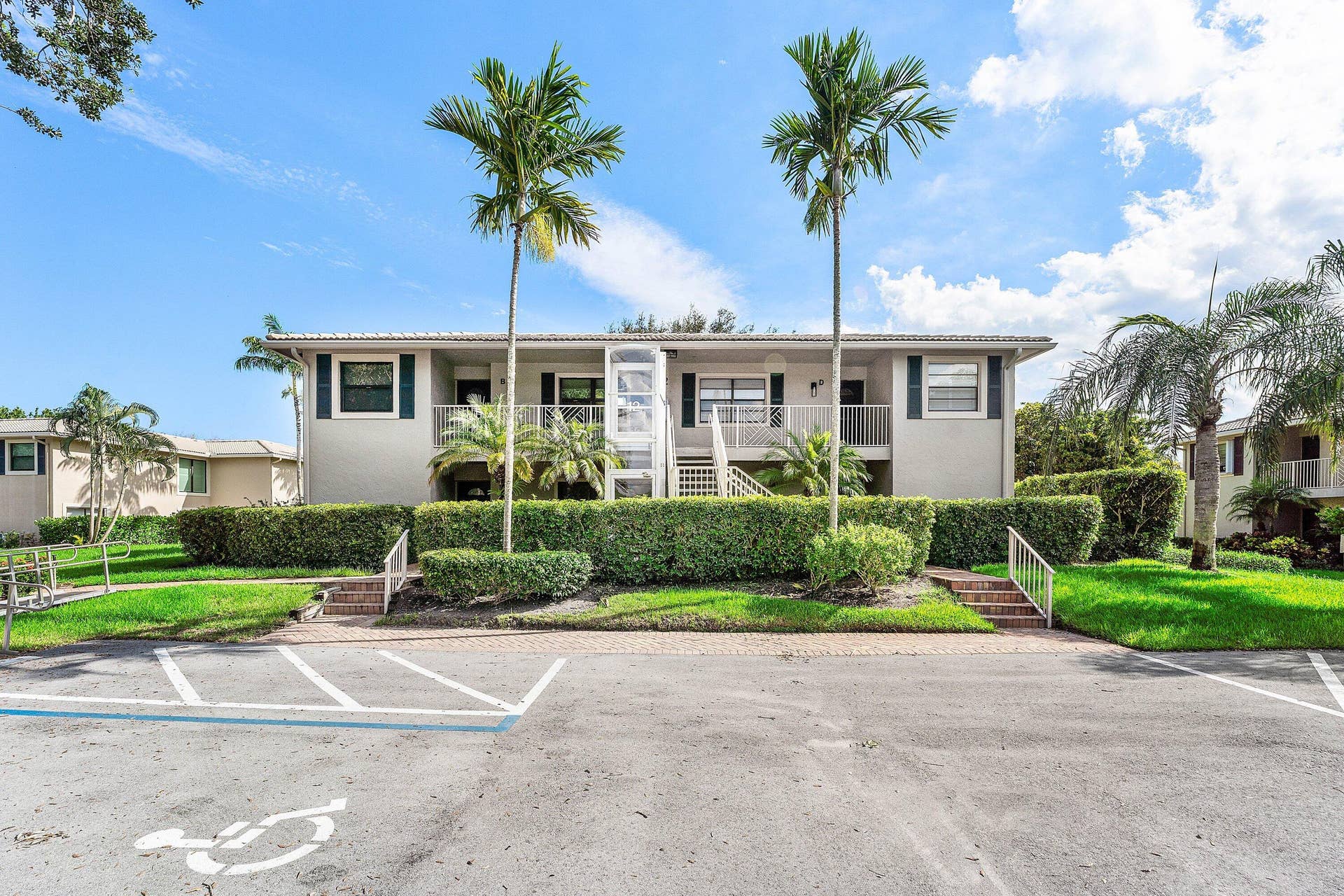 12 Stratford Drive E, #A, Boynton Beach, FL 33436 Two-story building with a light-colored stucco exterior, dark shutters, and white railings