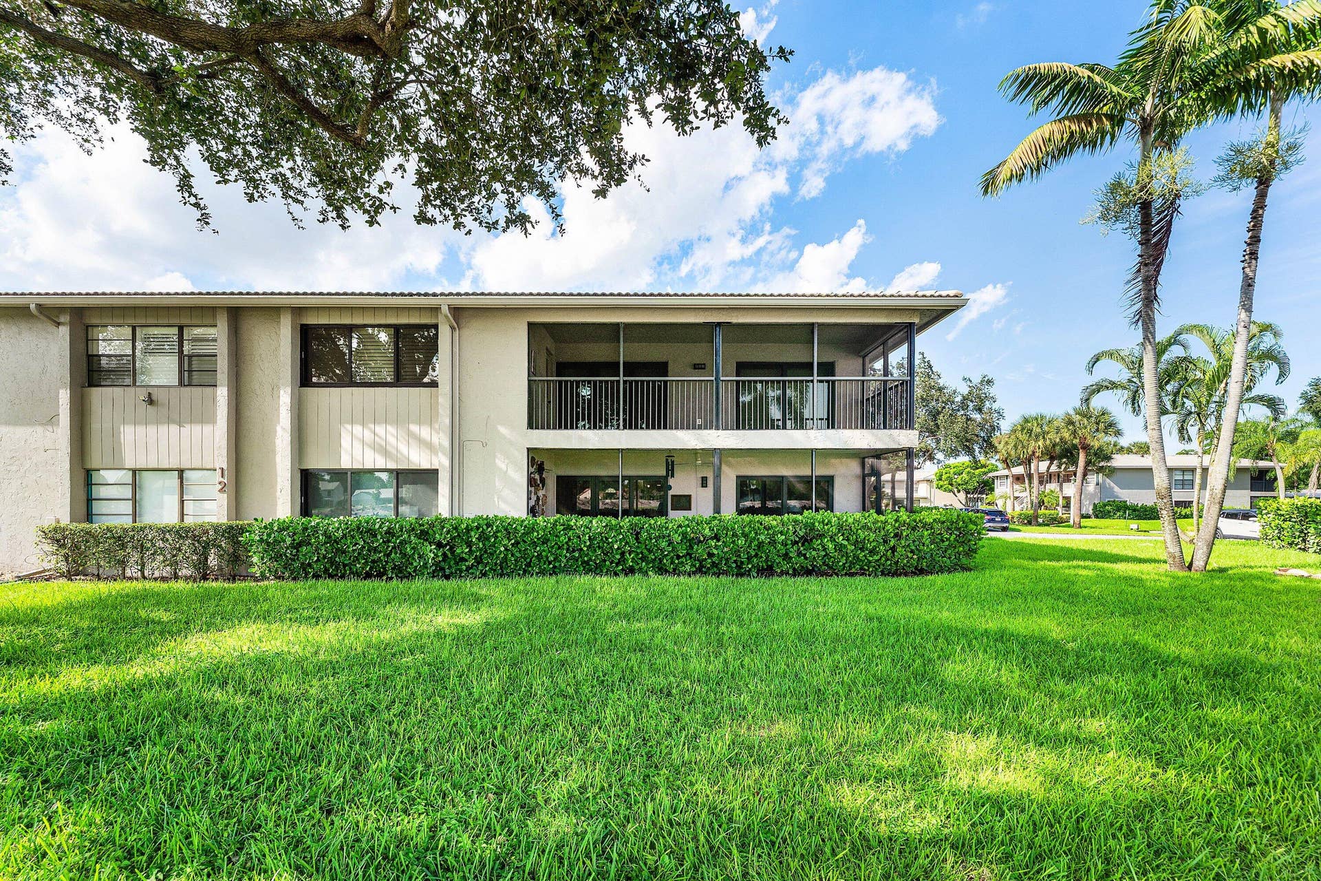 12 Stratford Drive E, #A, Boynton Beach, FL 33436 Exterior building featuring multiple screened balconies and patios, surrounded by mature landscaping and a well-maintained lawn