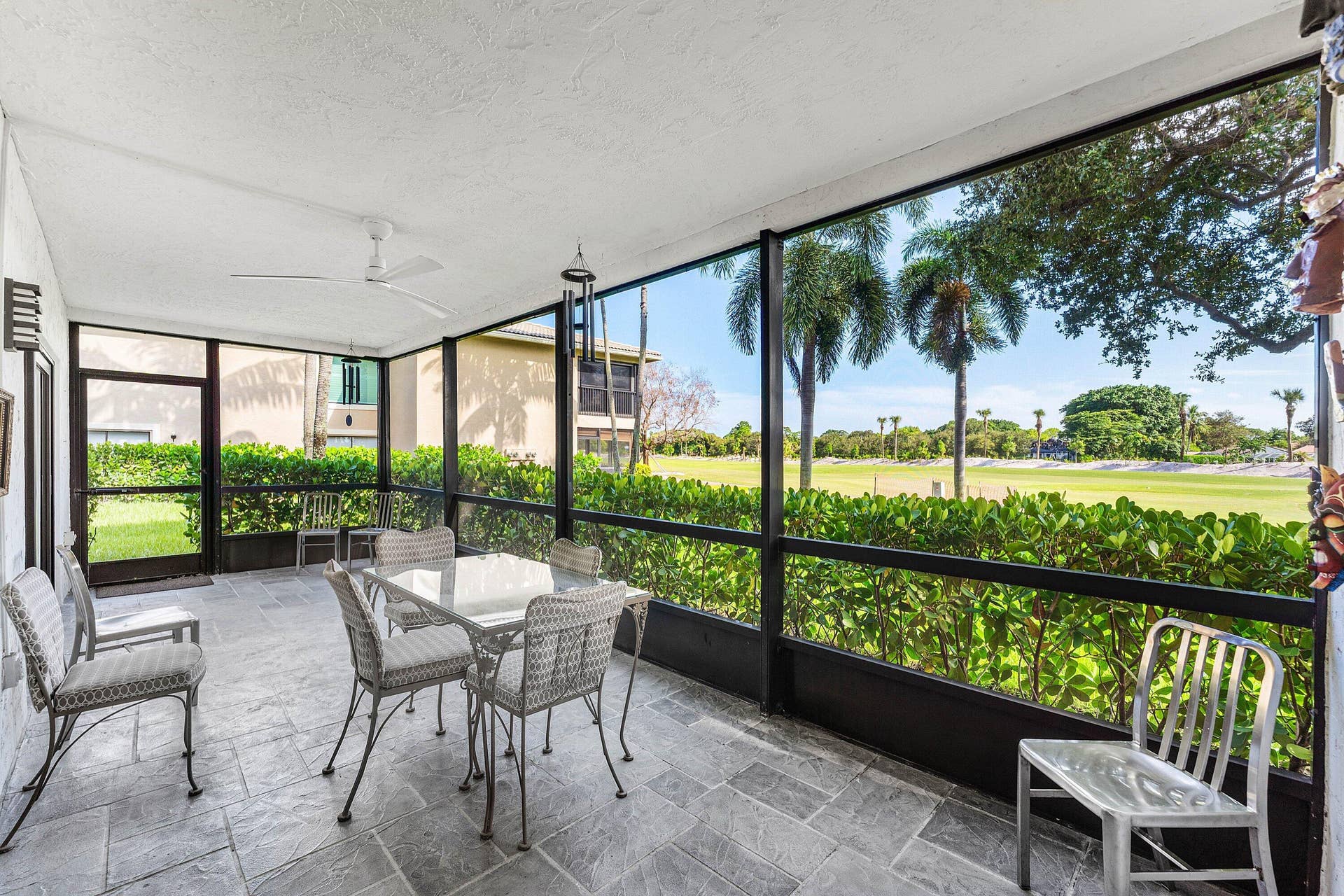 12 Stratford Drive E, #A, Boynton Beach, FL 33436 Screened outdoor living area with a ceiling fan, stone tile flooring, and direct access to outdoor greenspace