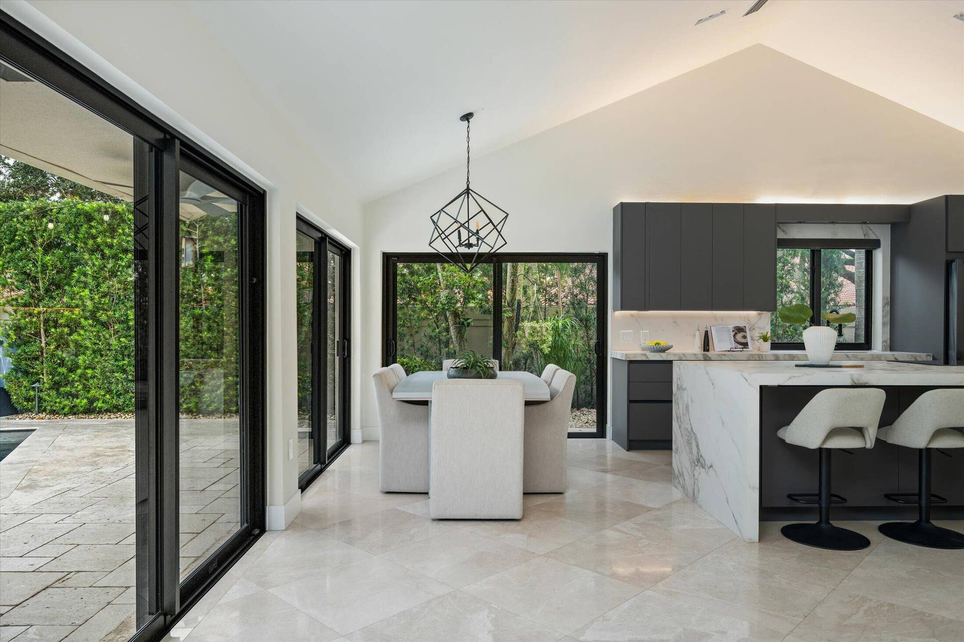 2890 ANTIETAM Lane, West Palm Beach, FL 33409 Vaulted ceiling with integrated lighting, expansive sliding glass doors, large format tile flooring, contemporary kitchen cabinetry, and a waterfall island with stone countertop
