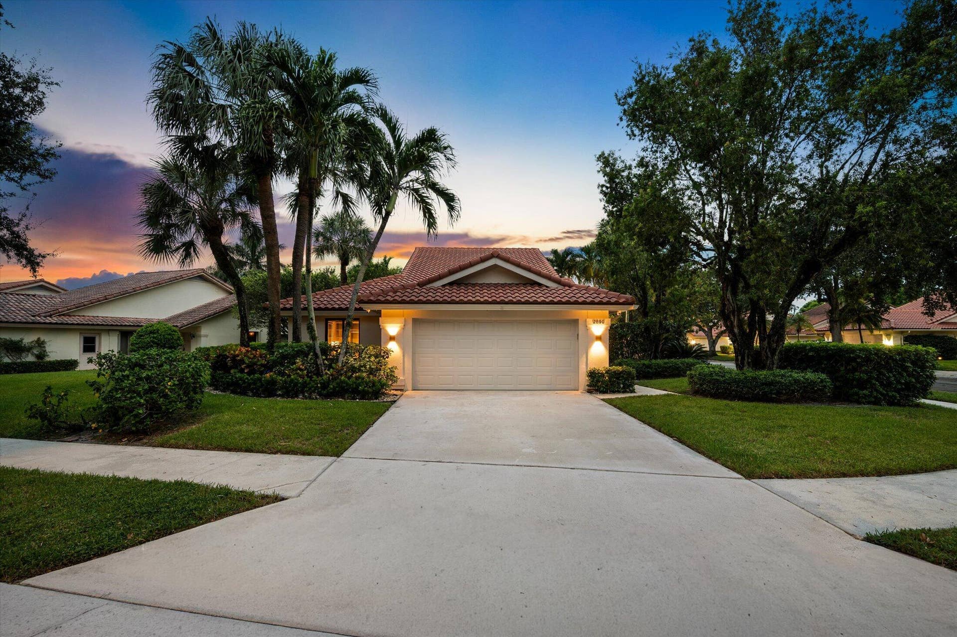 2890 ANTIETAM Lane, West Palm Beach, FL 33409 Mediterranean-style exterior featuring a tile roof, an integrated two-car garage, manicured landscaping, and a concrete driveway