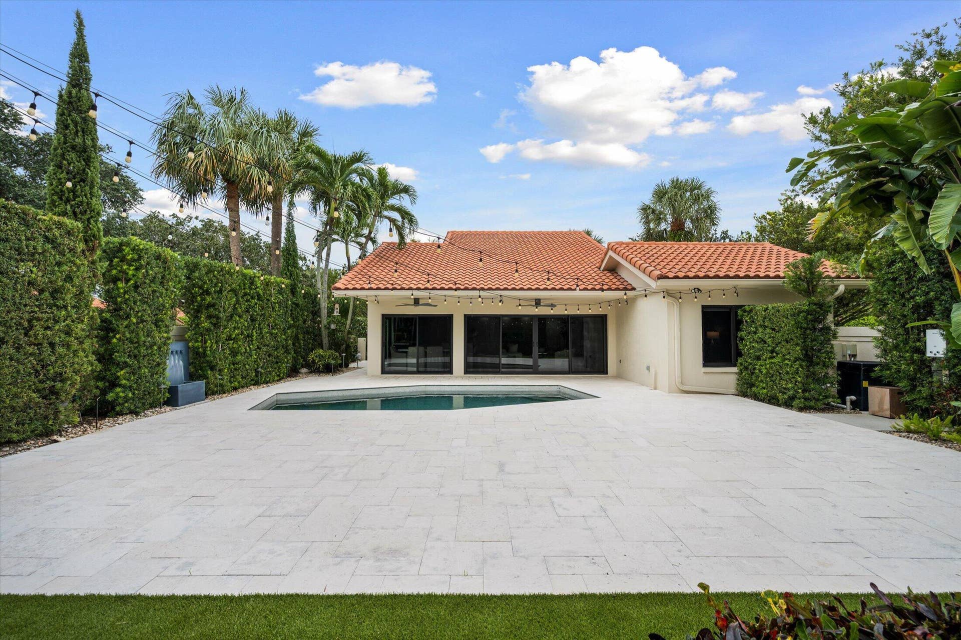 2890 ANTIETAM Lane, West Palm Beach, FL 33409 Terracotta tile roof, expansive paver patio, integrated swimming pool, mature privacy hedges, and lush tropical landscaping