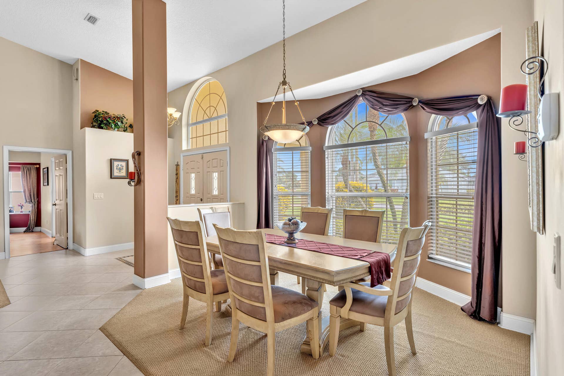 Arched windows with horizontal blinds, a decorative light fixture, and tile flooring
