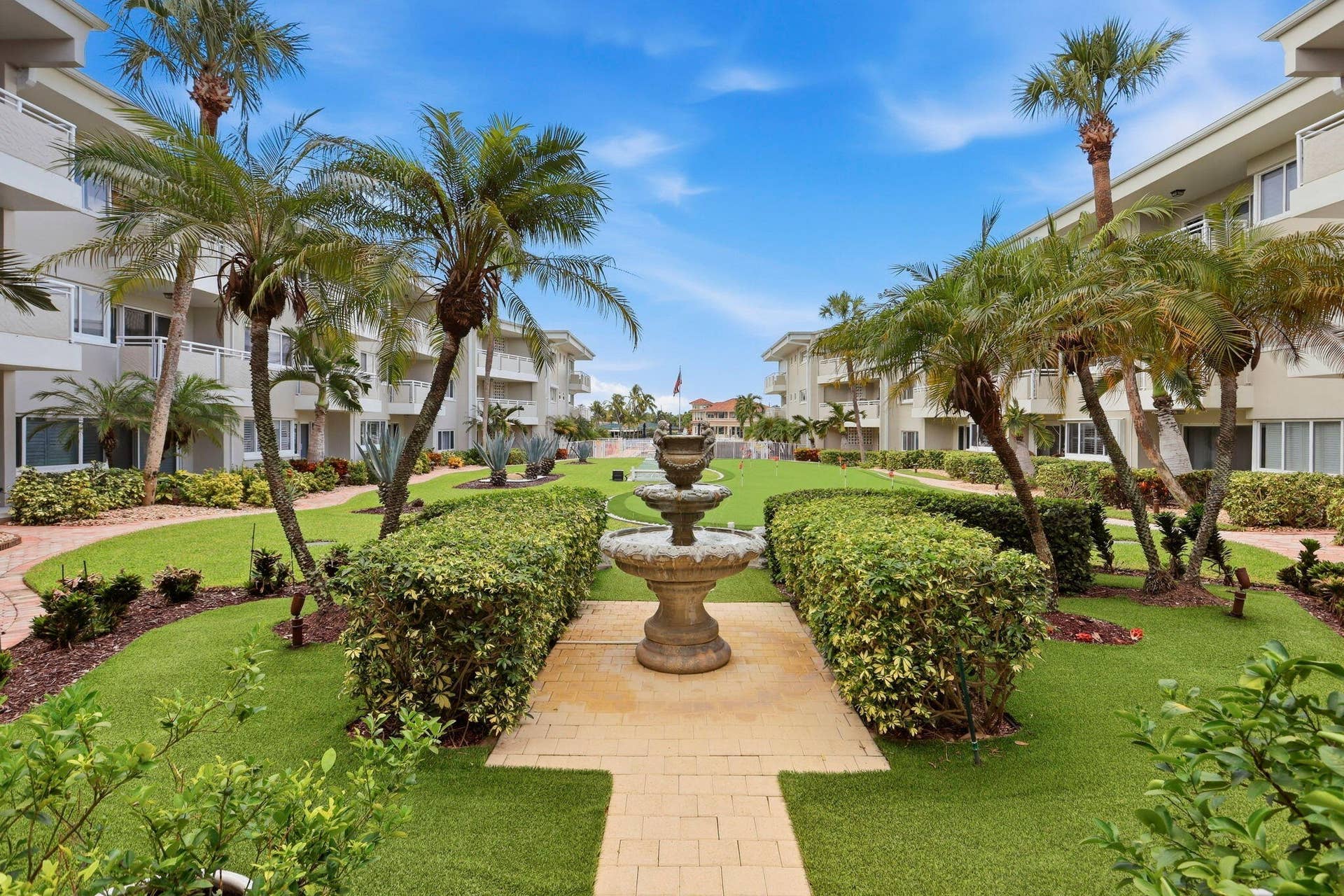 1198 Hillsboro Mile, #210, Hillsboro Beach, FL 33062 Landscaped courtyard featuring a tiered fountain, mature palm trees, manicured hedges, and paver pathways