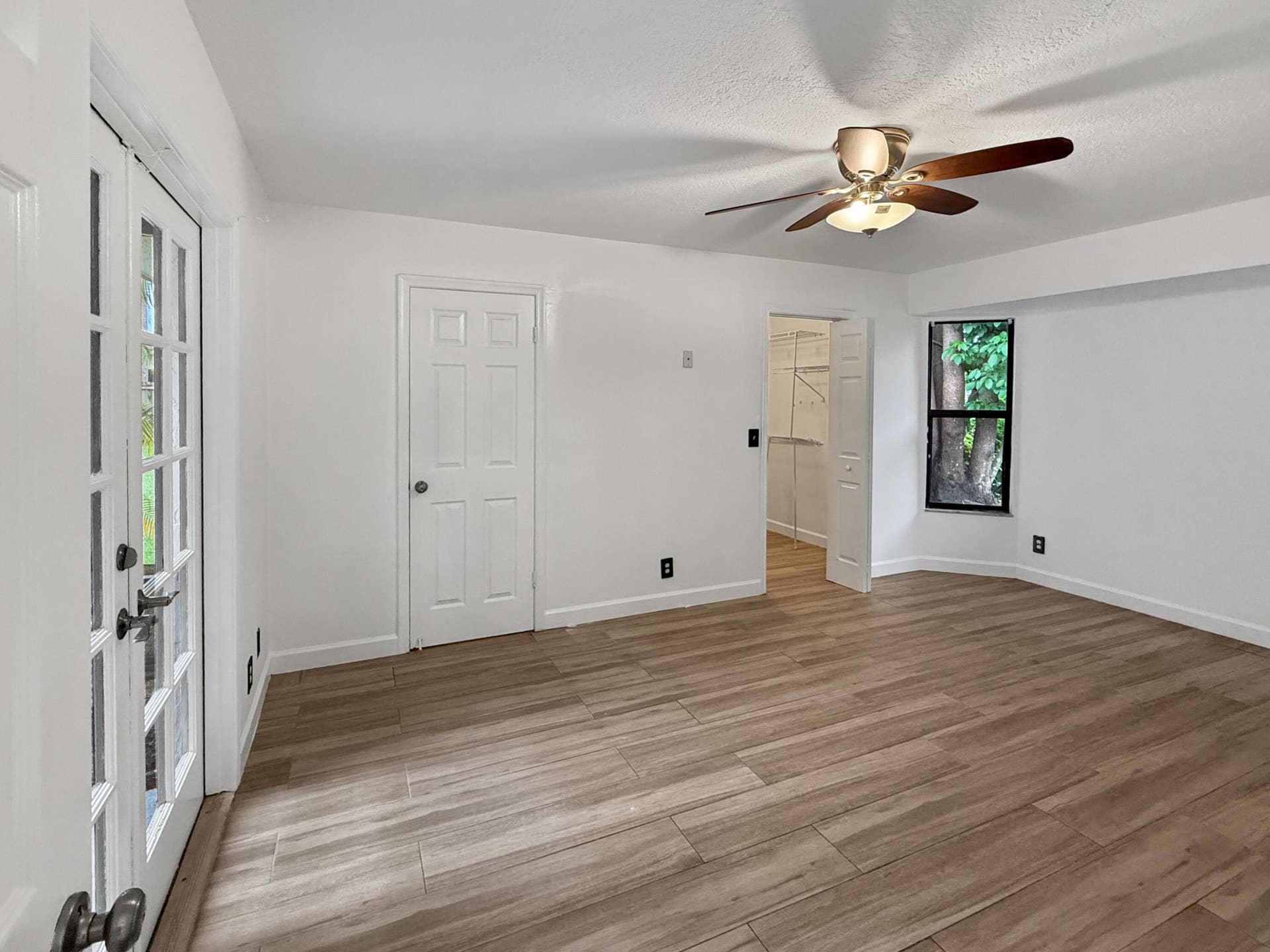 Wood-finish tile flooring, white walls, ceiling fan, French doors, and an additional doorway