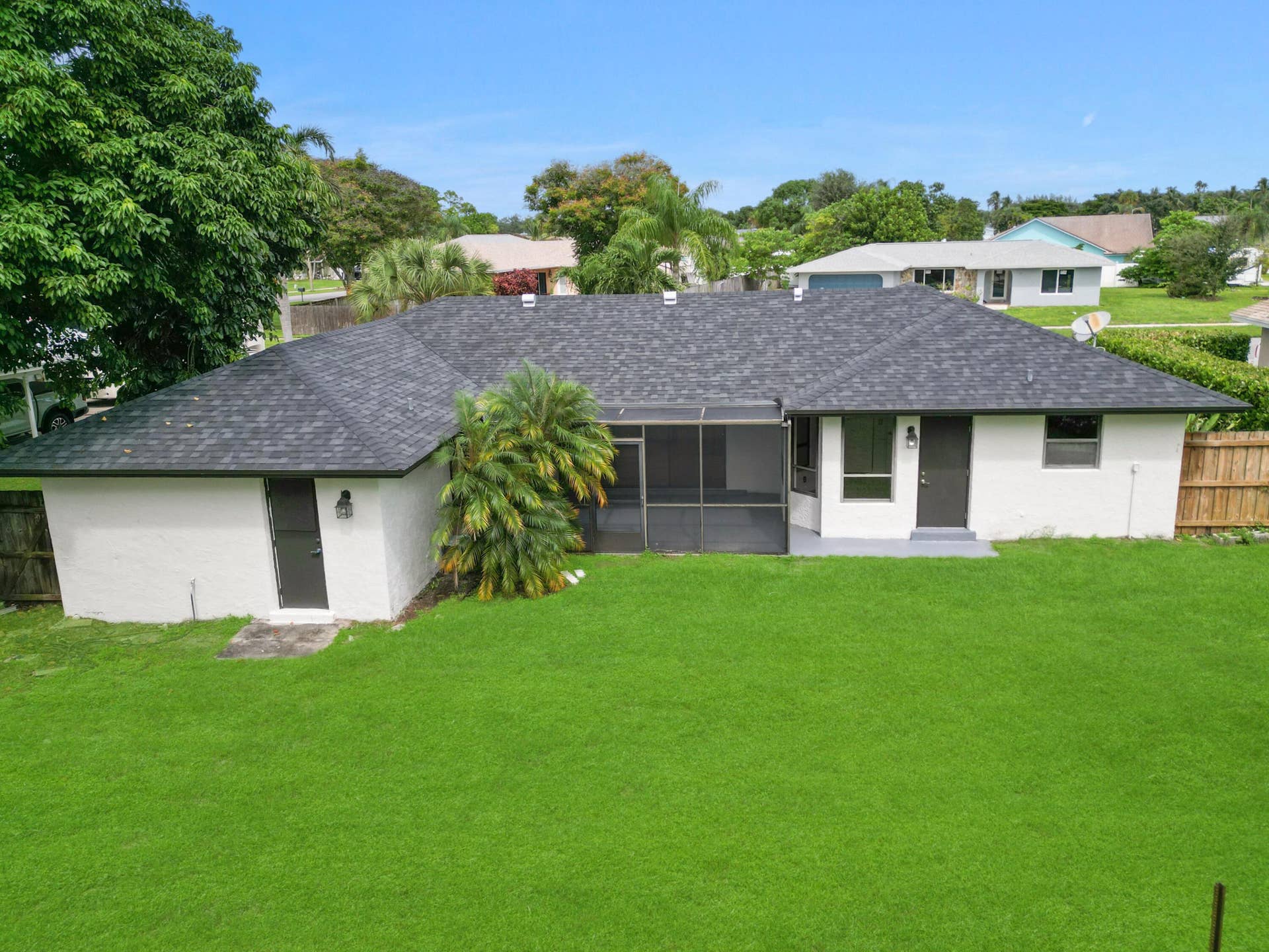 Expansive green lawn, dark shingle roof, screened patio, and exterior lighting fixtures