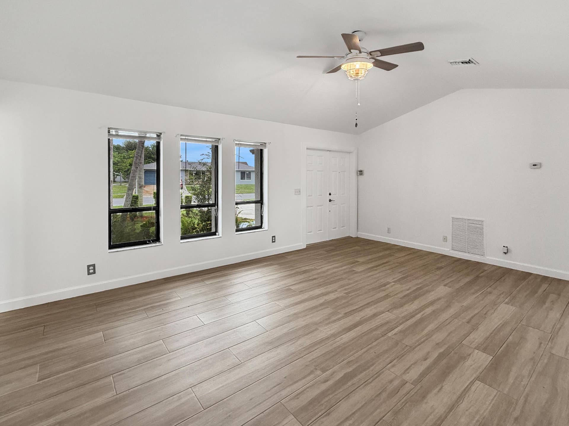 Vaulted ceilings, wood-finish flooring, three large windows, and a ceiling fan with light fixture