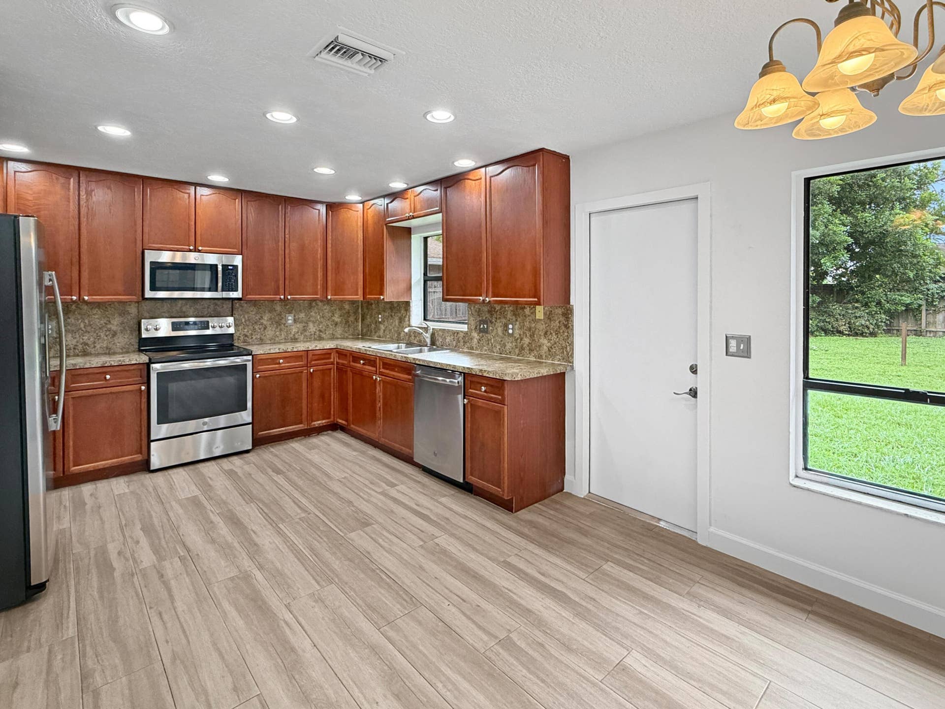 Kitchen featuring wood cabinetry, stainless steel appliances, recessed ceiling lights, stone-finish countertops, and wood-finish flooring
