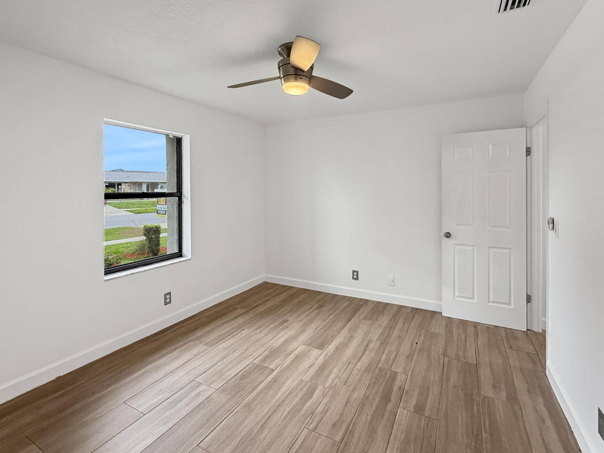 Bright corner bedroom featuring wood-finish flooring, a ceiling fan with integrated lighting, large window with natural light, and white six-panel closet door with chrome hardware
