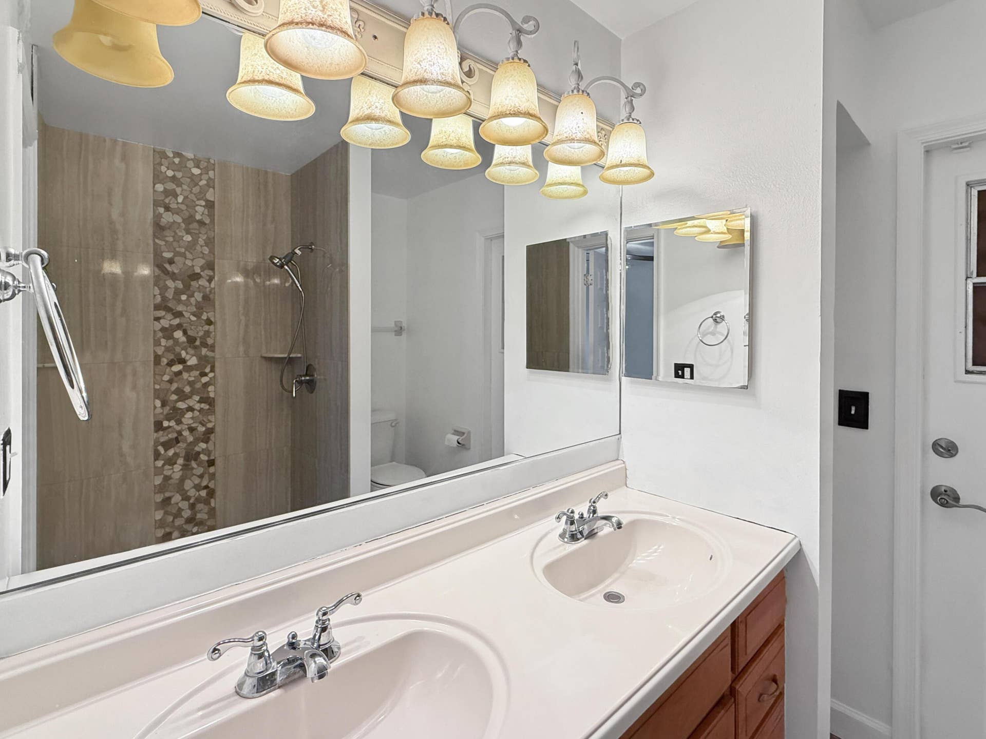Double vanity with integrated sinks, wood-finish cabinetry, chrome fixtures, and overhead sconce lighting