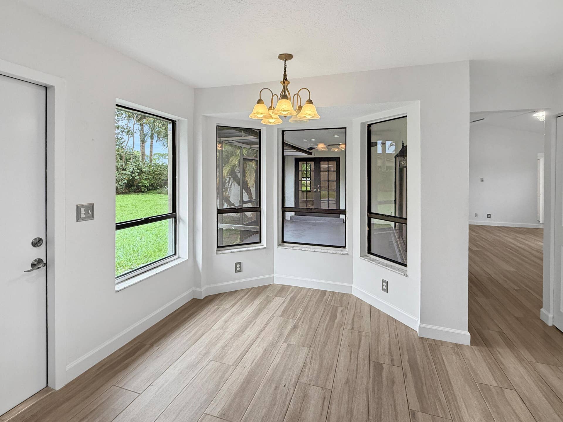 Bay window with ample natural light, wood-finish tileflooring, and a decorative chandelier