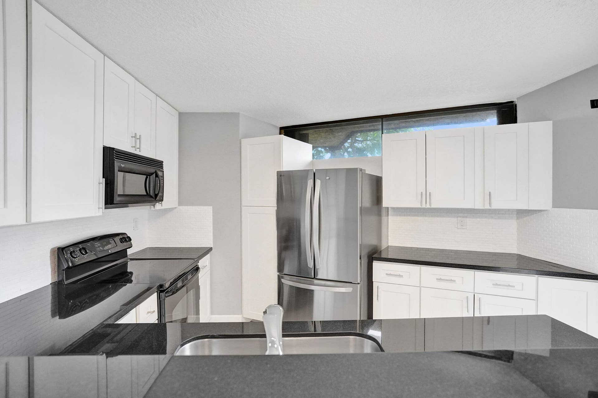 Kitchen featuring white cabinetry, black countertops, stainless steel refrigerator,