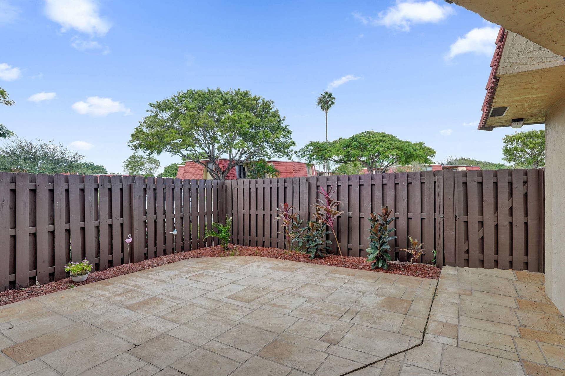 Paved patio area with a privacy fence and garden beds.